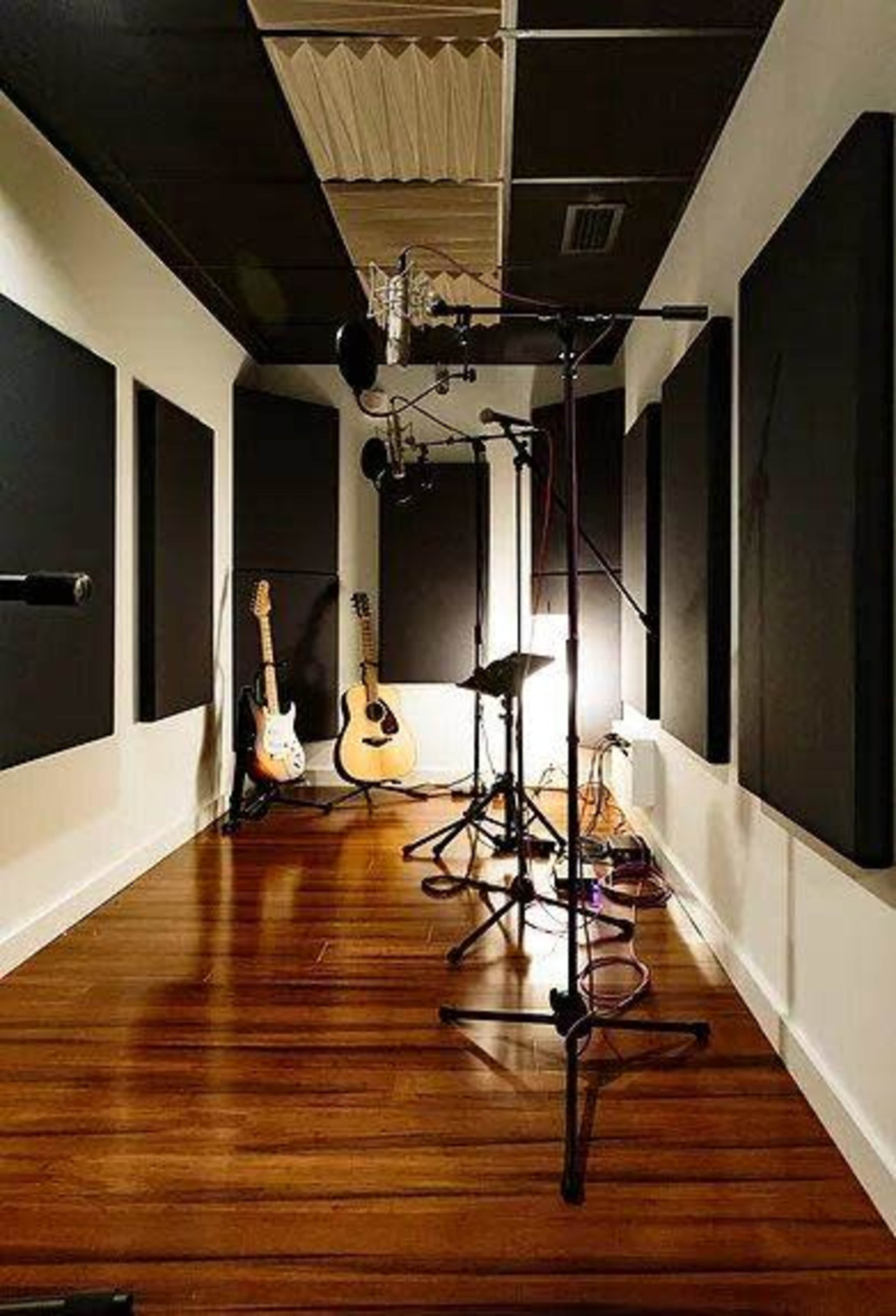 A recording studio with soundproofed walls, microphones set up, and various musical instruments, including electric and acoustic guitars.