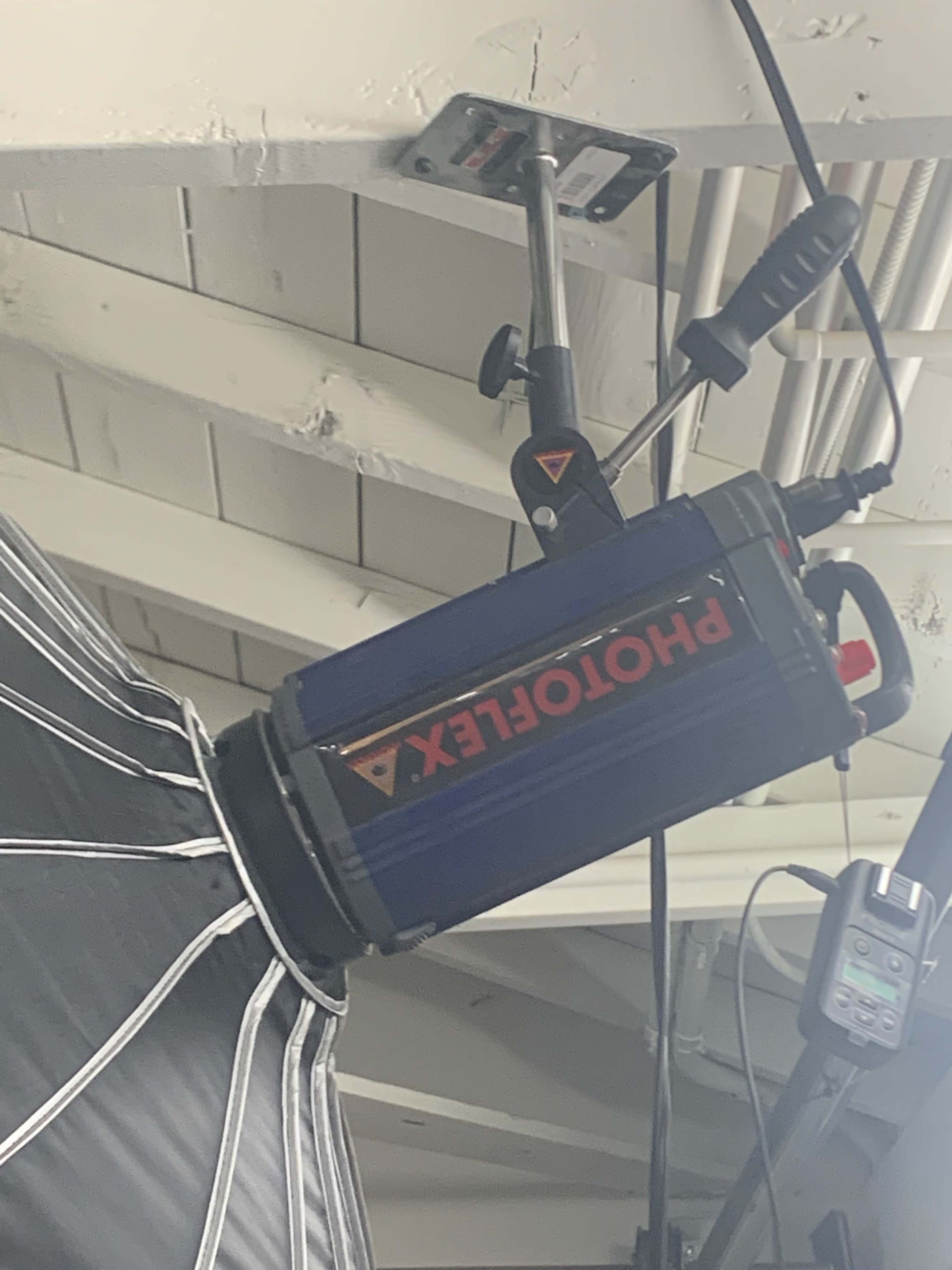 A mounted studio light with a softbox attached, hanging from a white ceiling beam.