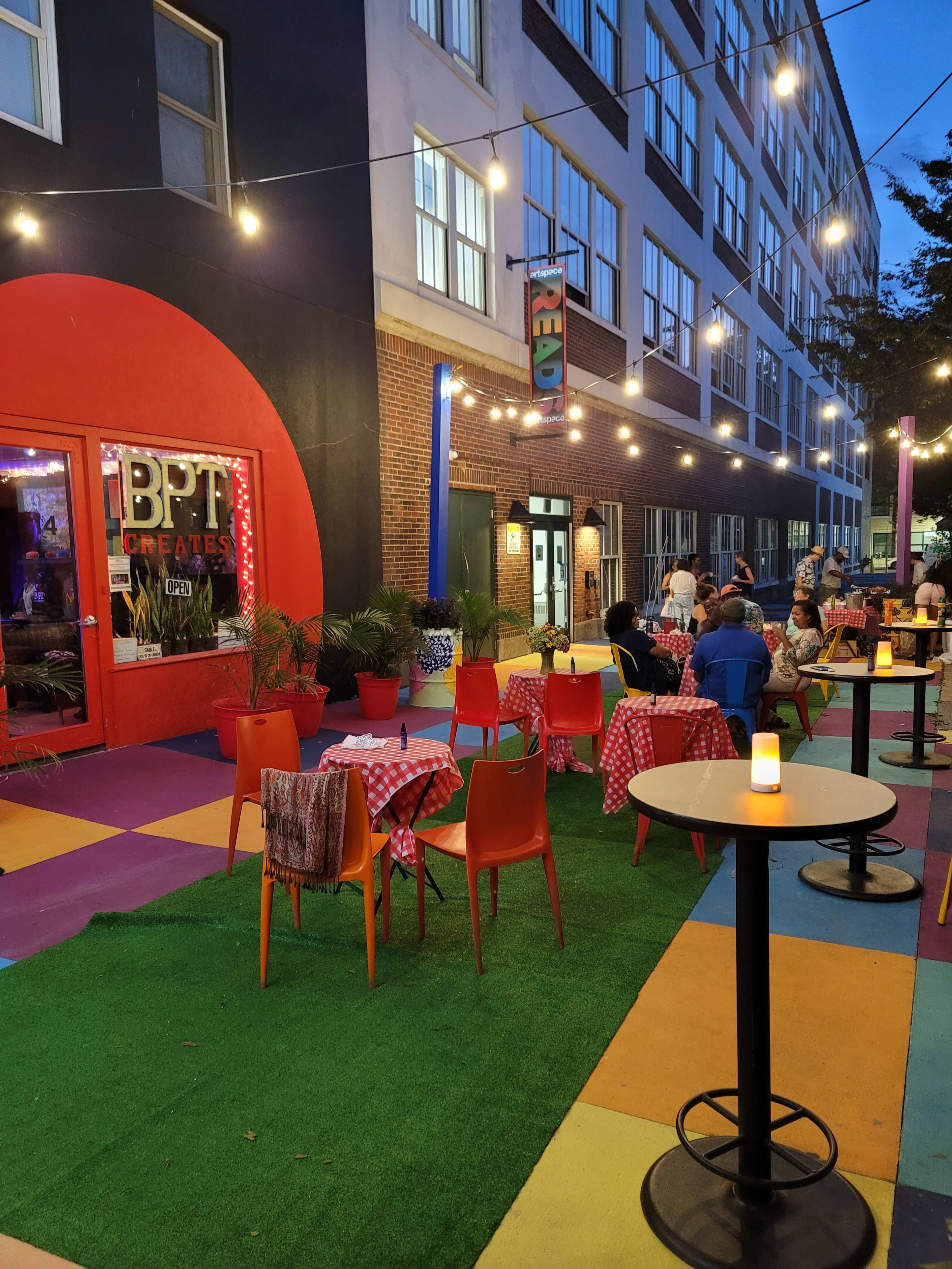 An outdoor dining area with colorful table settings and string lights in front of a restaurant.