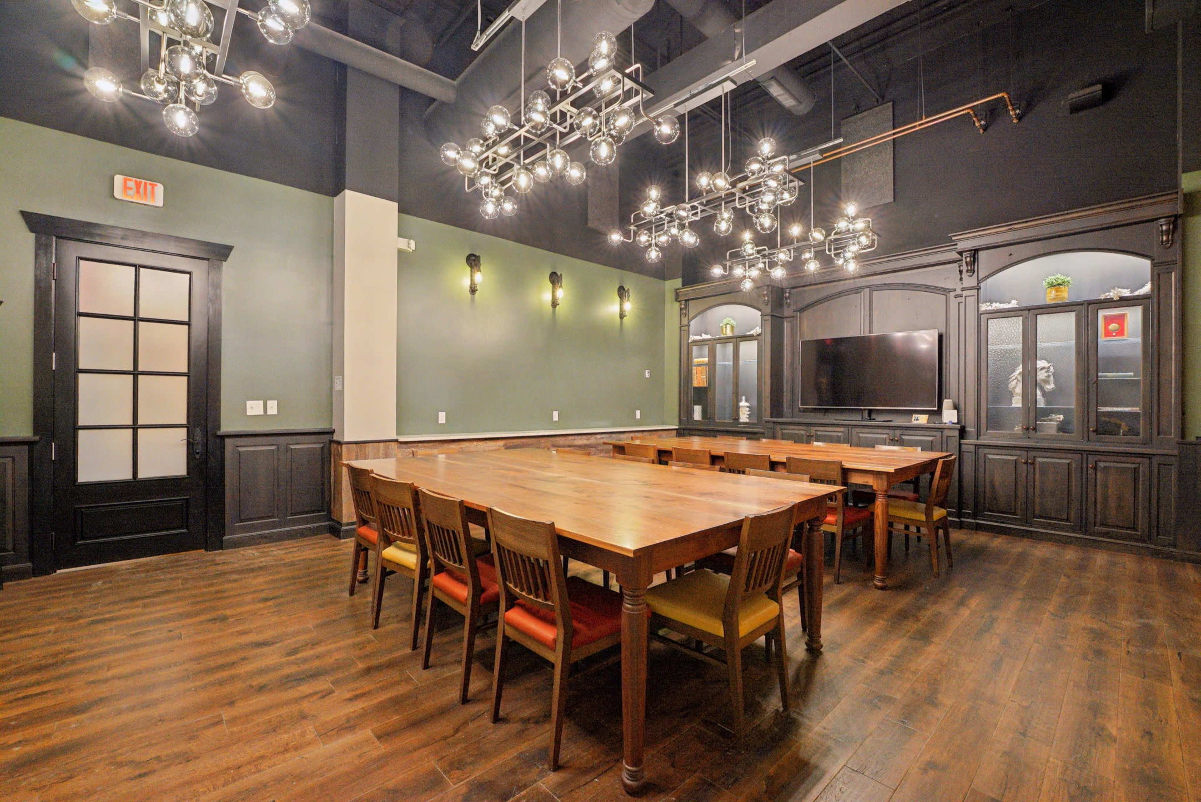 The image shows a conference room with a long wooden table surrounded by chairs and modern chandelier lighting above.