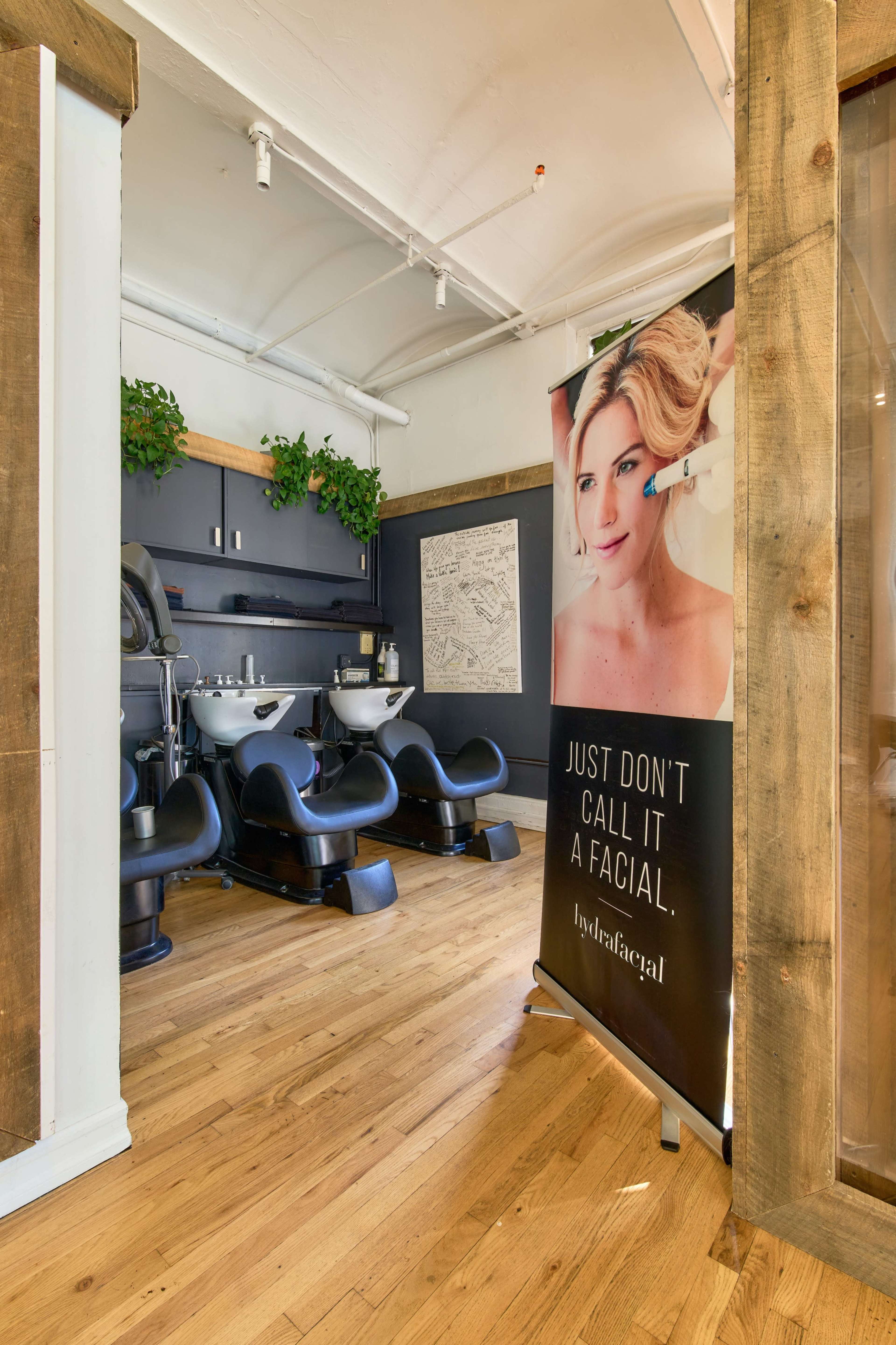 The image shows a modern spa interior featuring two salon wash stations and a promotional banner for hydrafacial services.