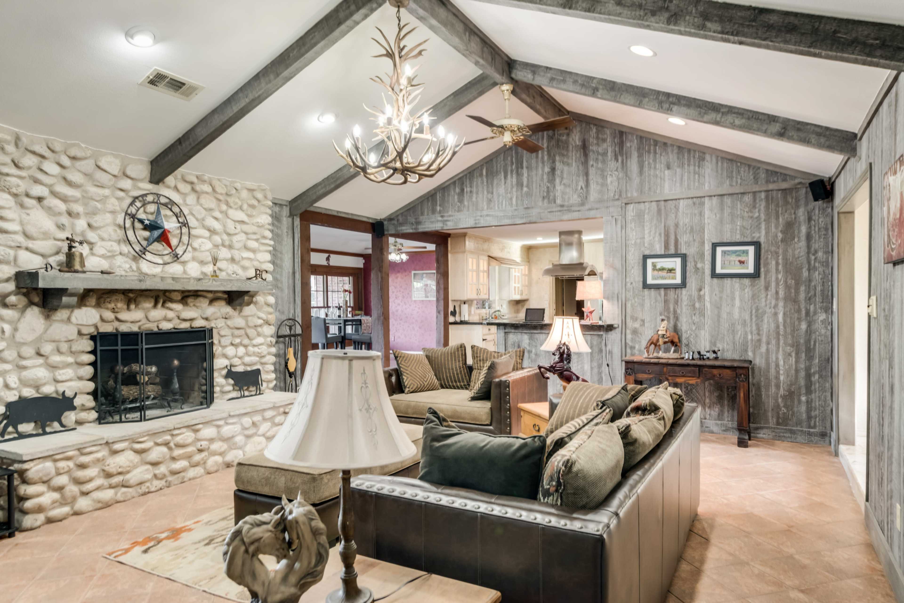 The image shows a living room with a stone fireplace, wooden beams, and comfortable seating arranged around a coffee table.