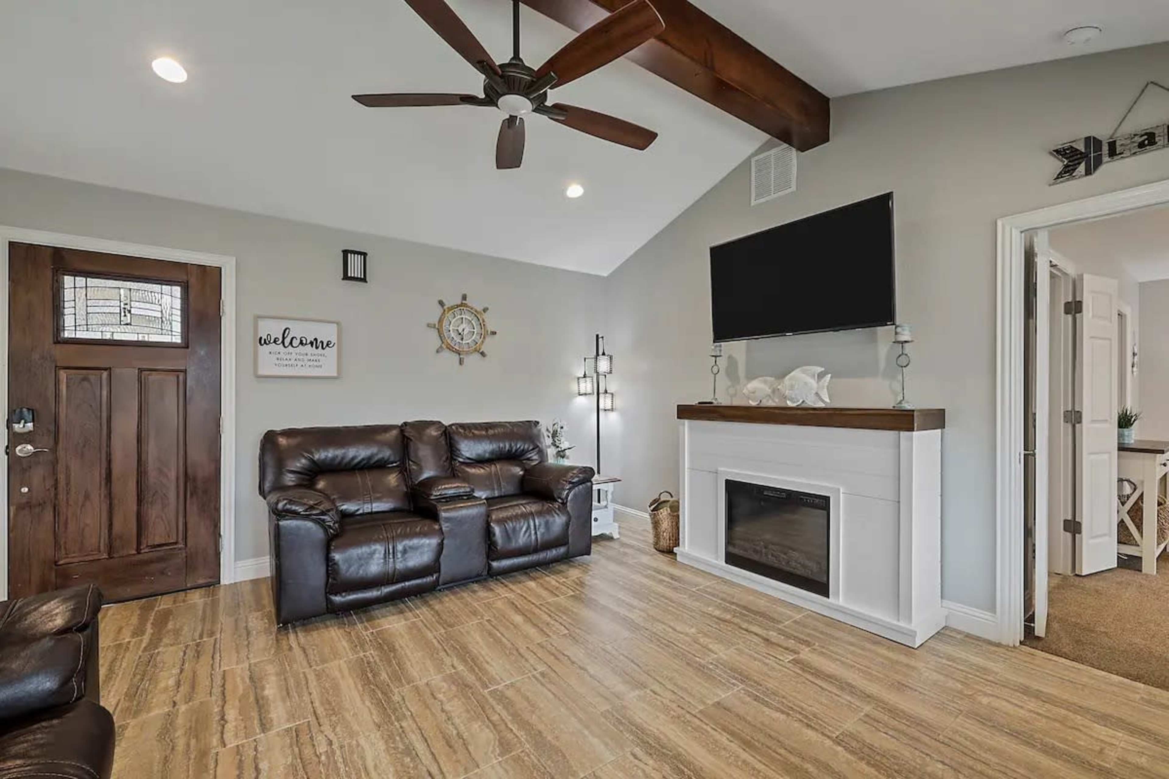 A living room featuring leather sofas, a wall-mounted television, a decorative fireplace, and a wooden door with a welcome sign.