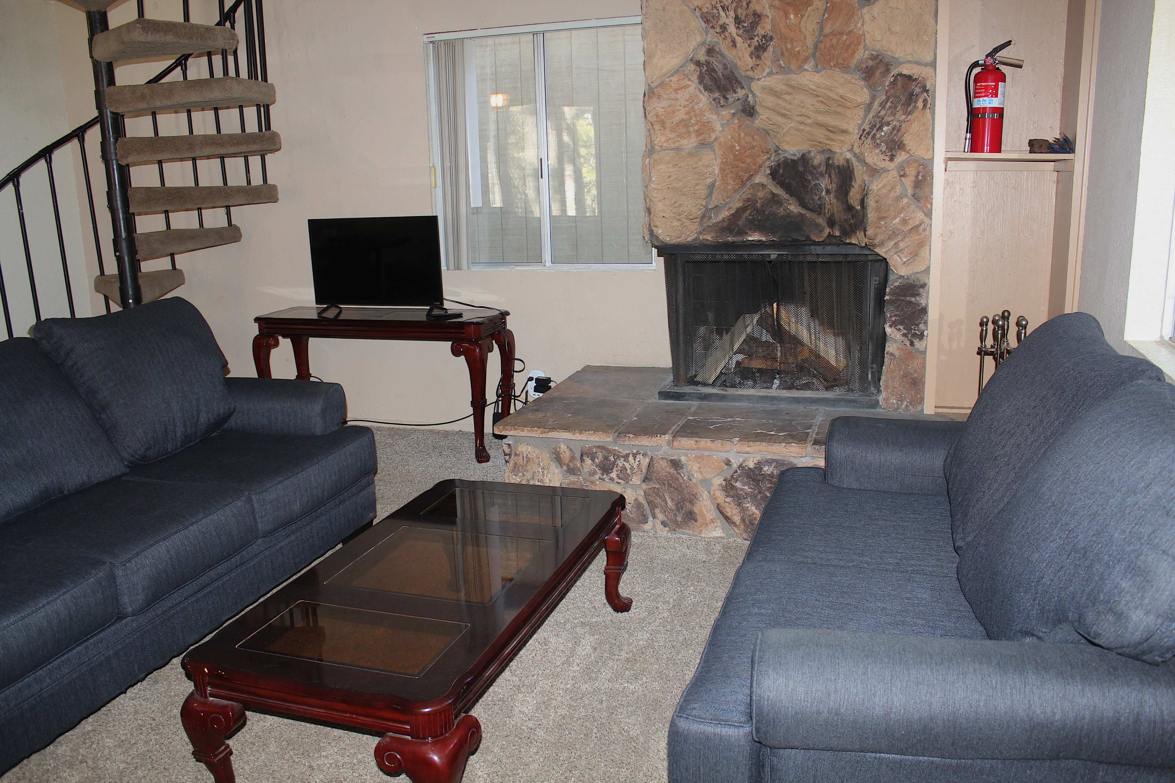 The living room features two blue sofas facing a coffee table, with a stone fireplace and a television on a wooden stand nearby.