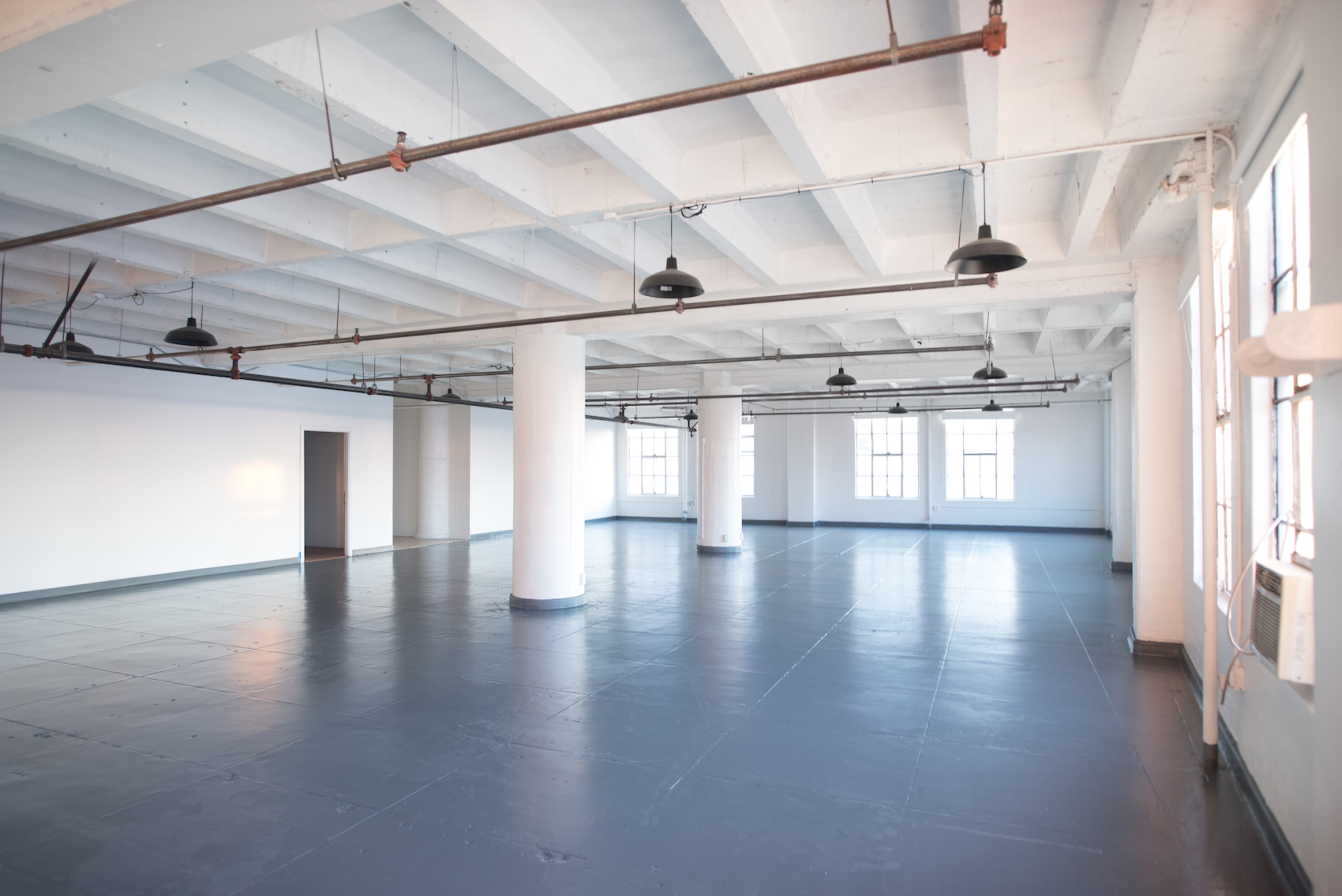 A large, empty industrial-style room with high ceilings, concrete columns, and multiple windows.