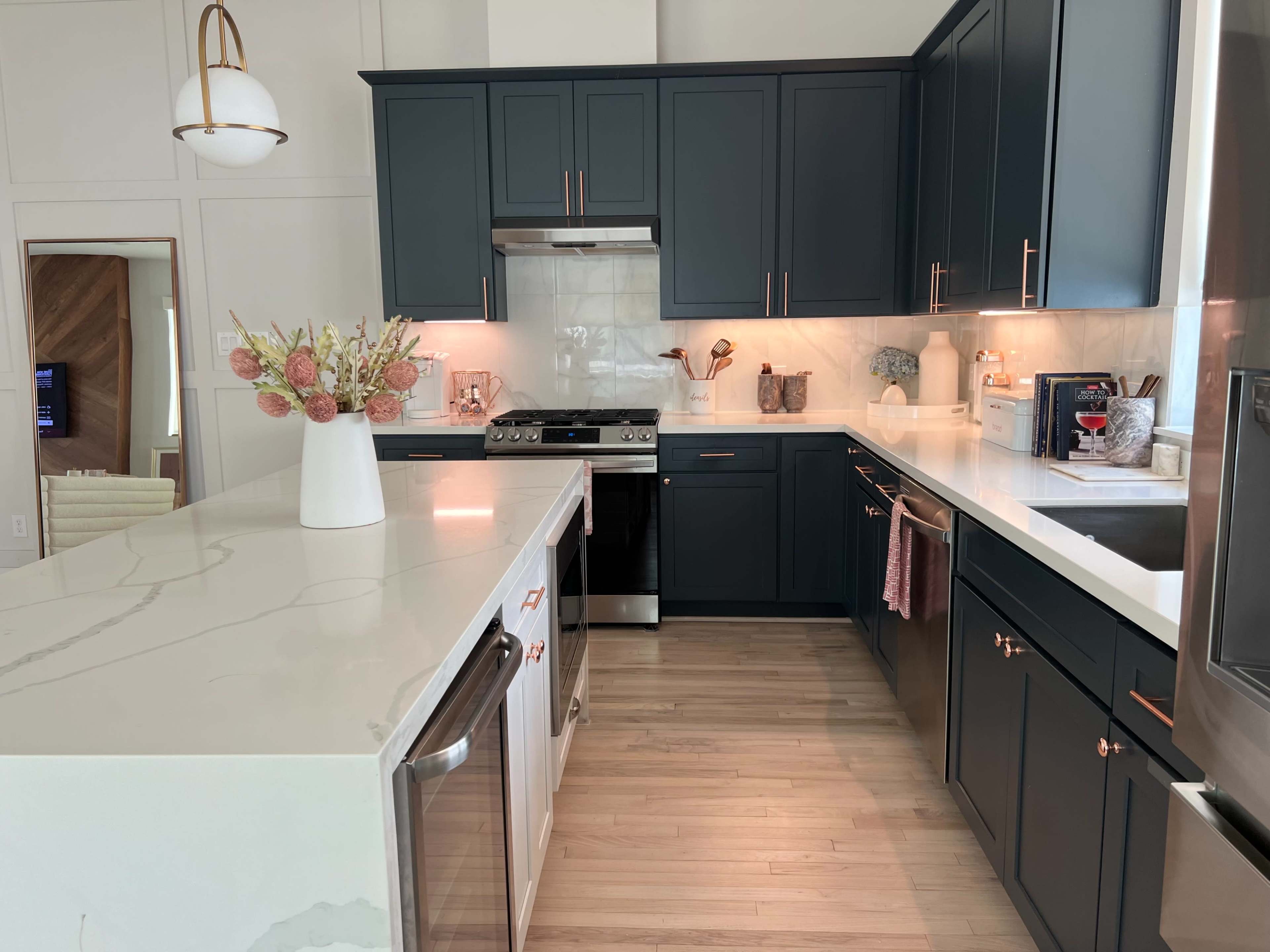 The kitchen features dark cabinets, a large white countertop, stainless steel appliances, and decorative vases on display.