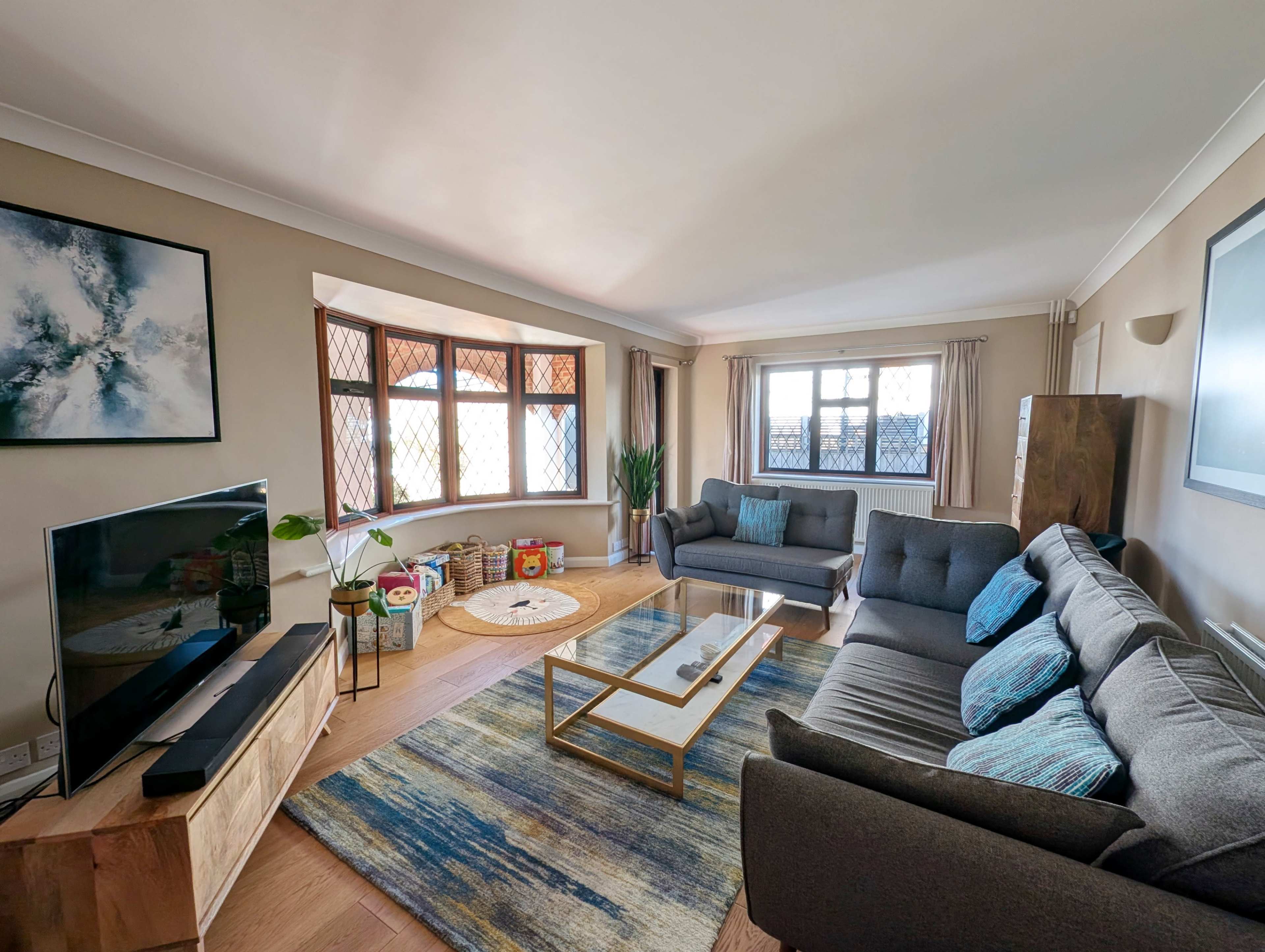 A spacious living room features a comfortable seating arrangement, a large window, a television, and a coffee table on a colorful rug.
