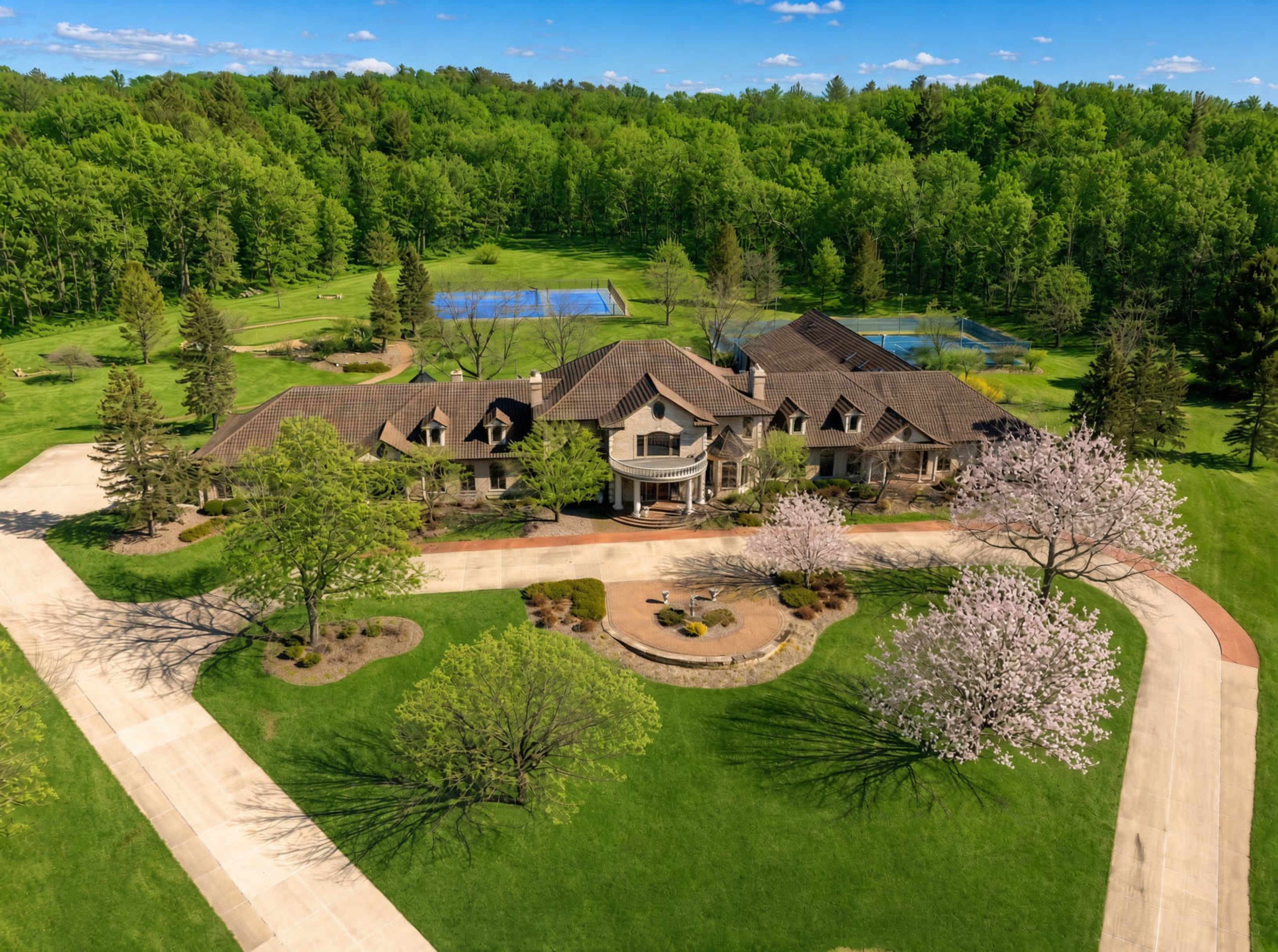 The image shows a large, elegantly designed house surrounded by green trees and a manicured lawn, with a tennis court visible in the background.