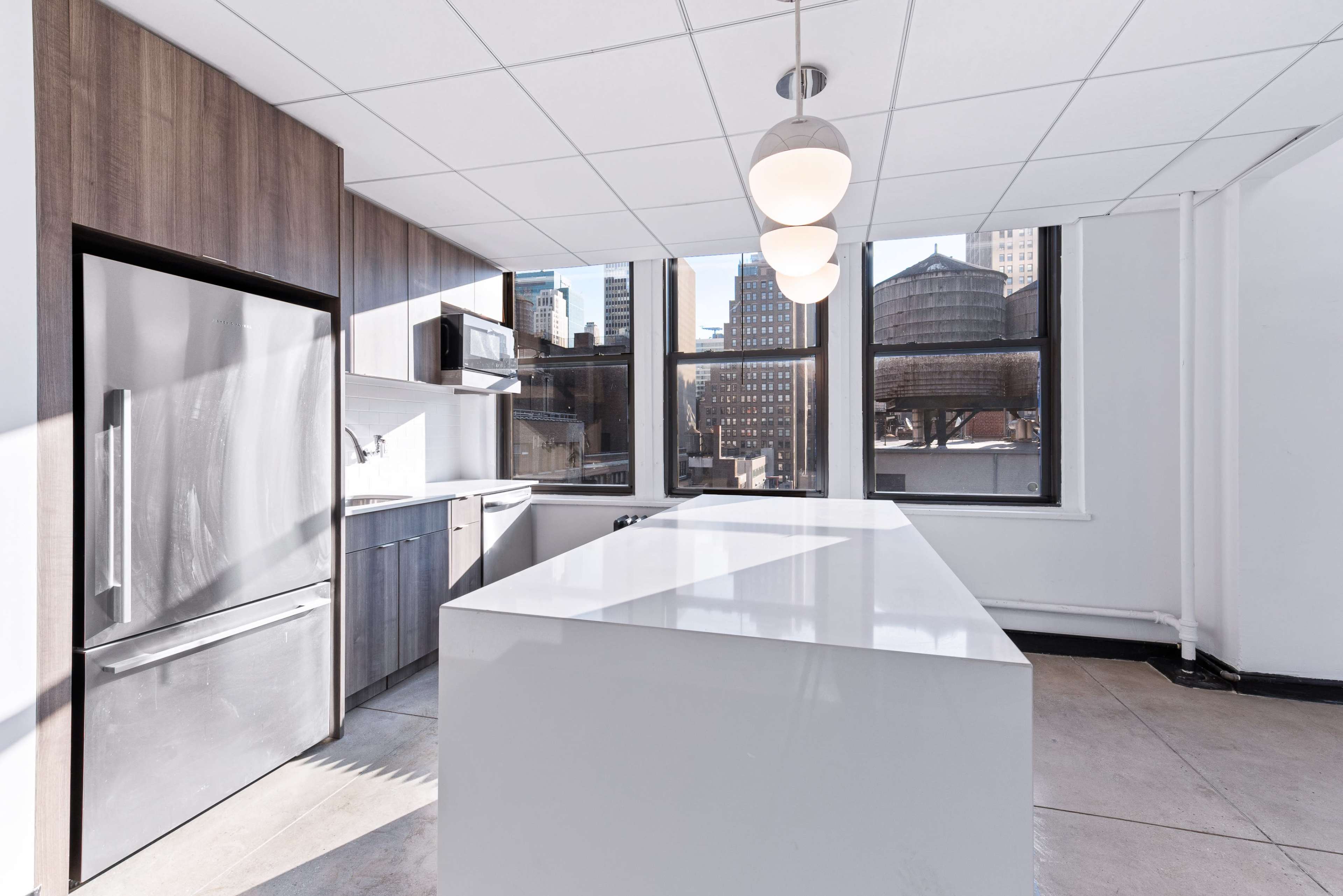 A modern kitchen with a large island, stainless steel appliances, and multiple windows overlooking a cityscape.