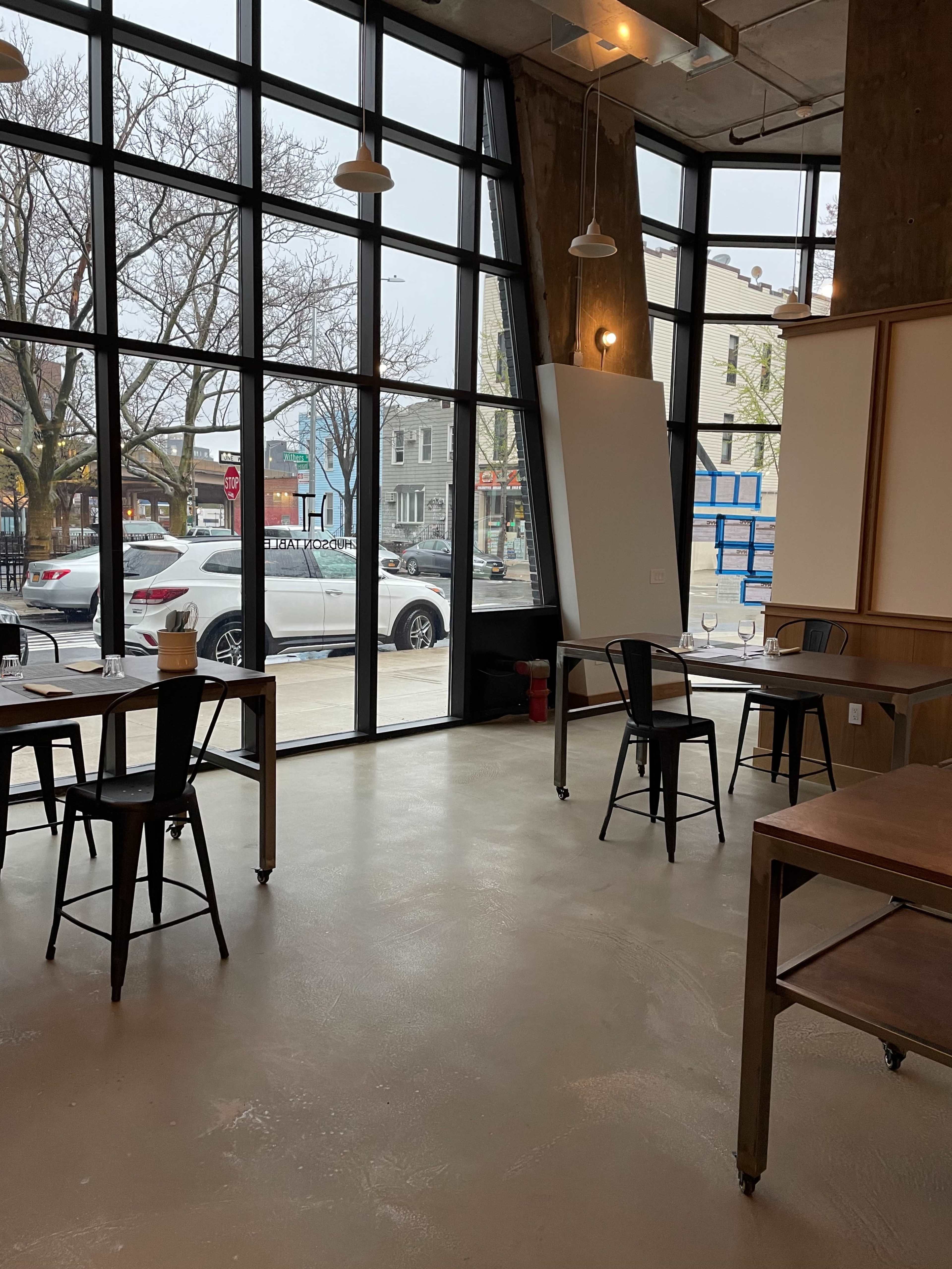 A spacious, modern café with large windows, several tables, and a view of cars parked outside.