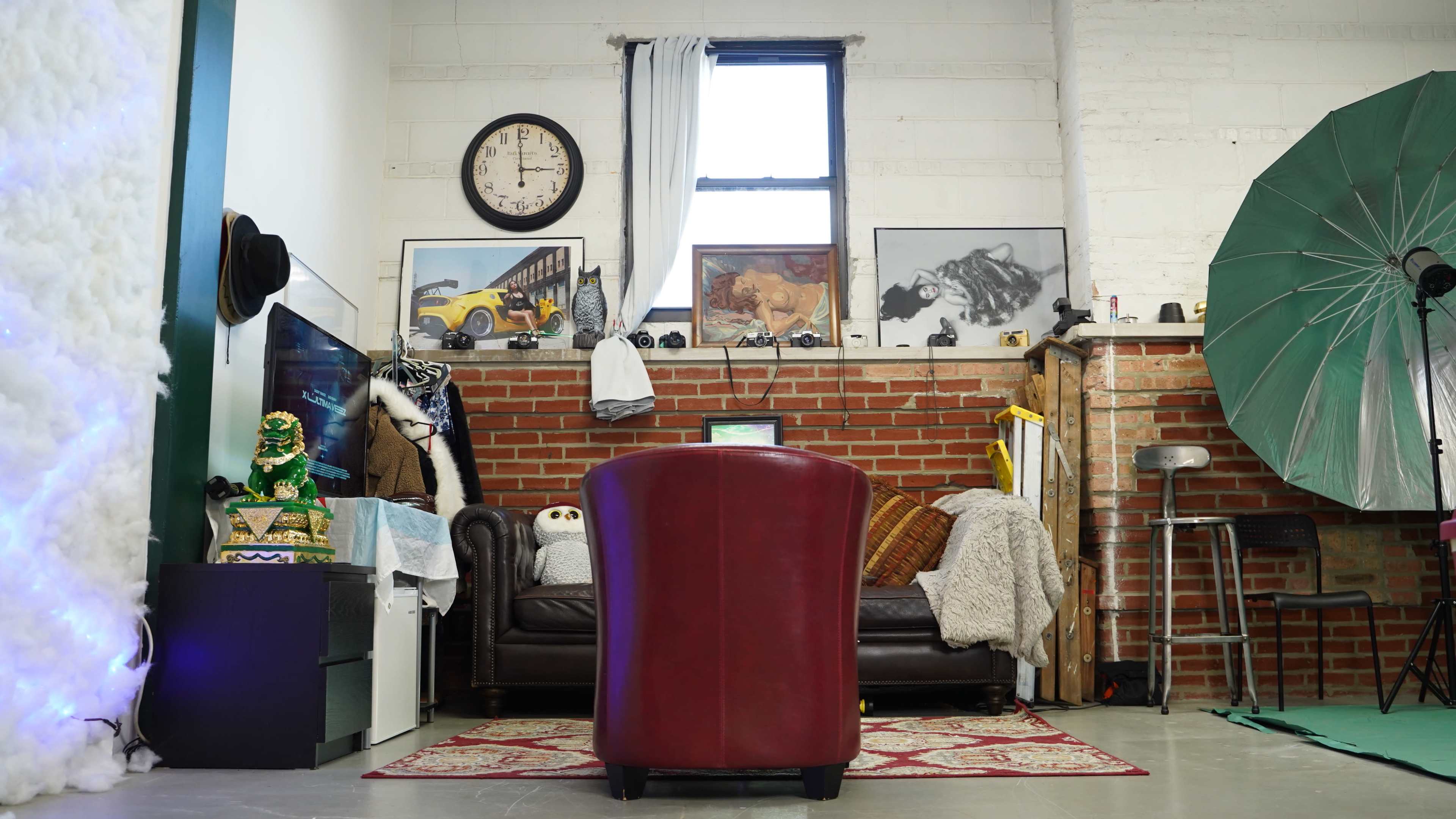 A cozy interior with a red chair facing a brown leather couch, surrounded by various decorations, a wall clock, and artwork displayed on the walls.