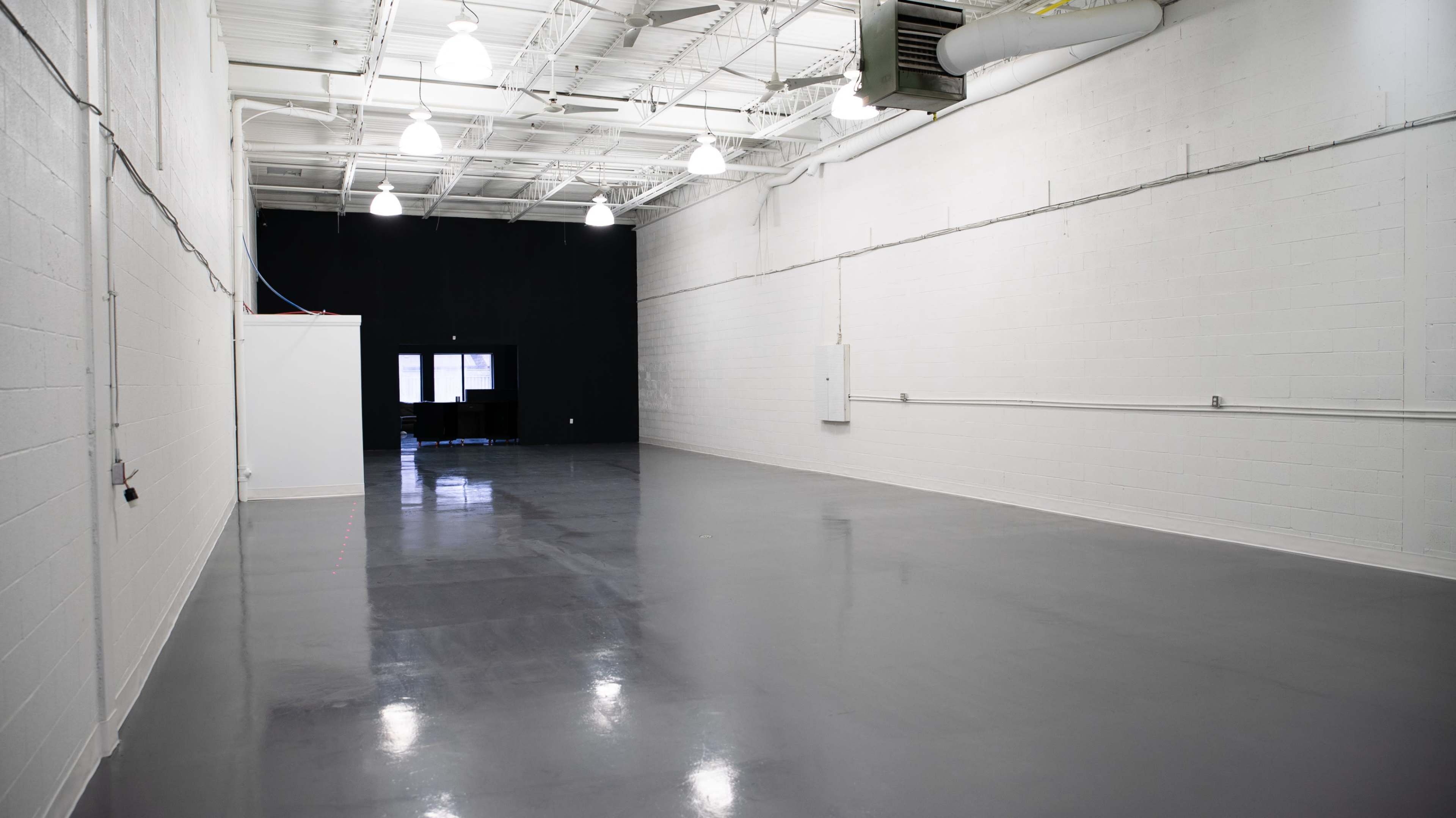 A large, empty indoor space with white walls, a polished gray floor, and a black wall at one end.