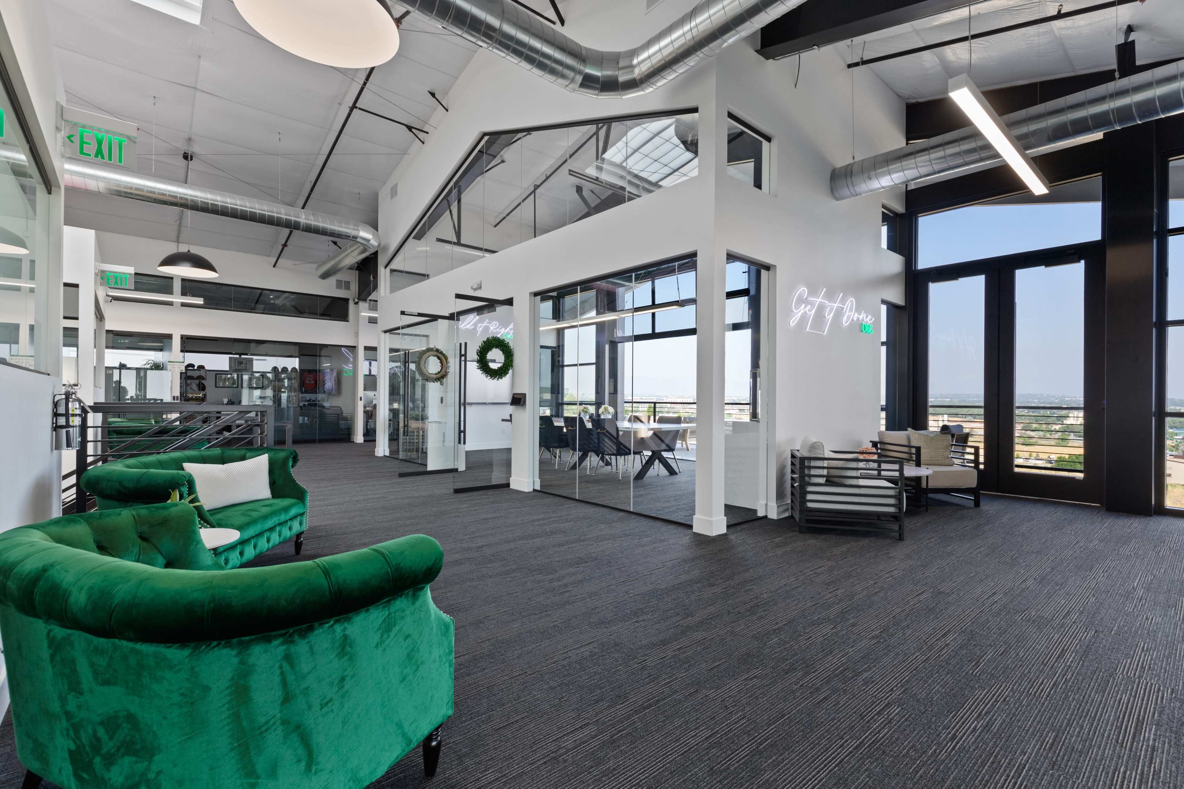 The image shows a modern office interior with green velvet seating, large windows, and an open layout featuring metal accents and white walls.