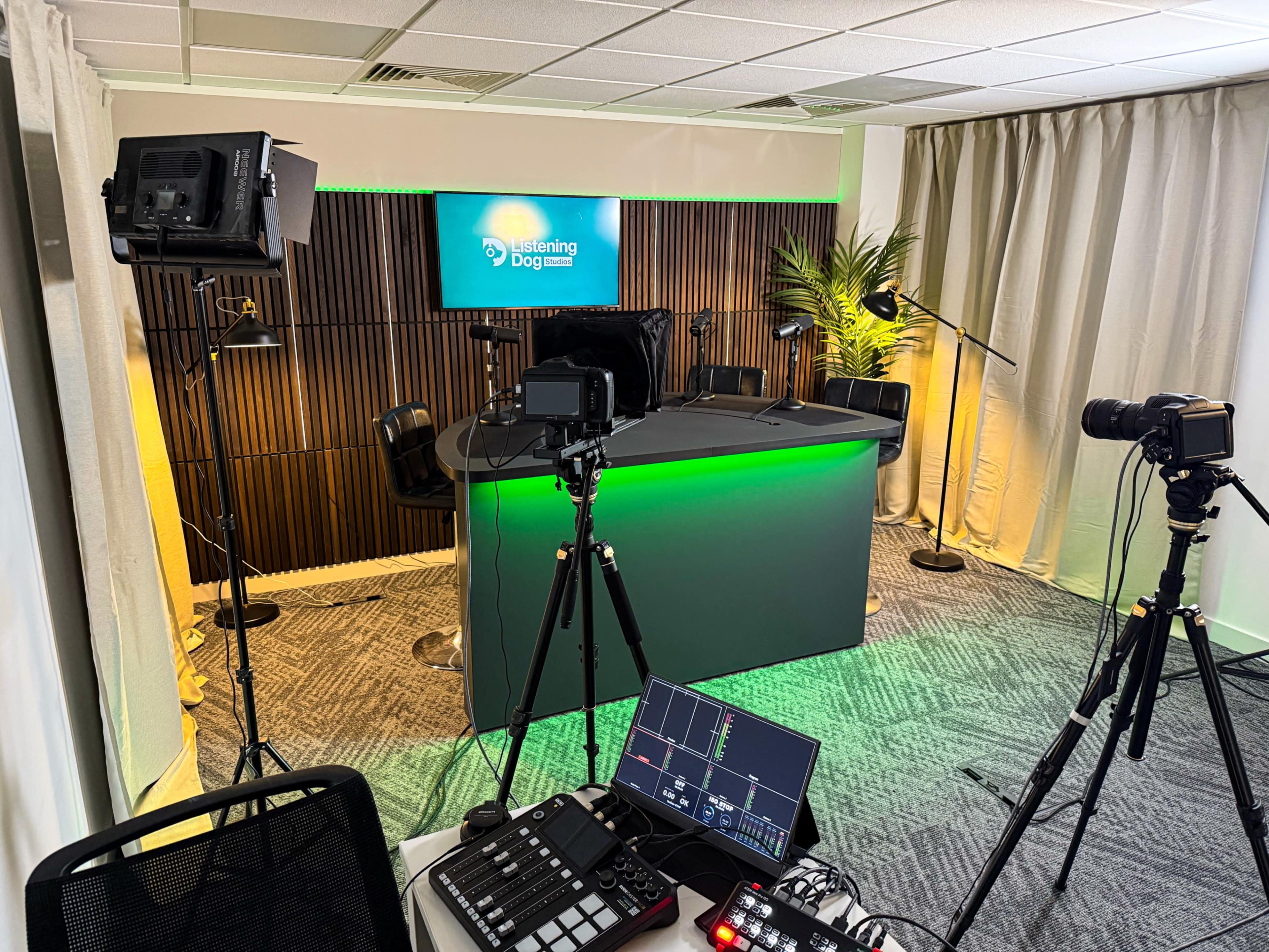 The image shows a modern studio setup with a dark, illuminated desk, multiple cameras on tripods, and lighting equipment, along with a screen displaying the logo of "Listening Dog."