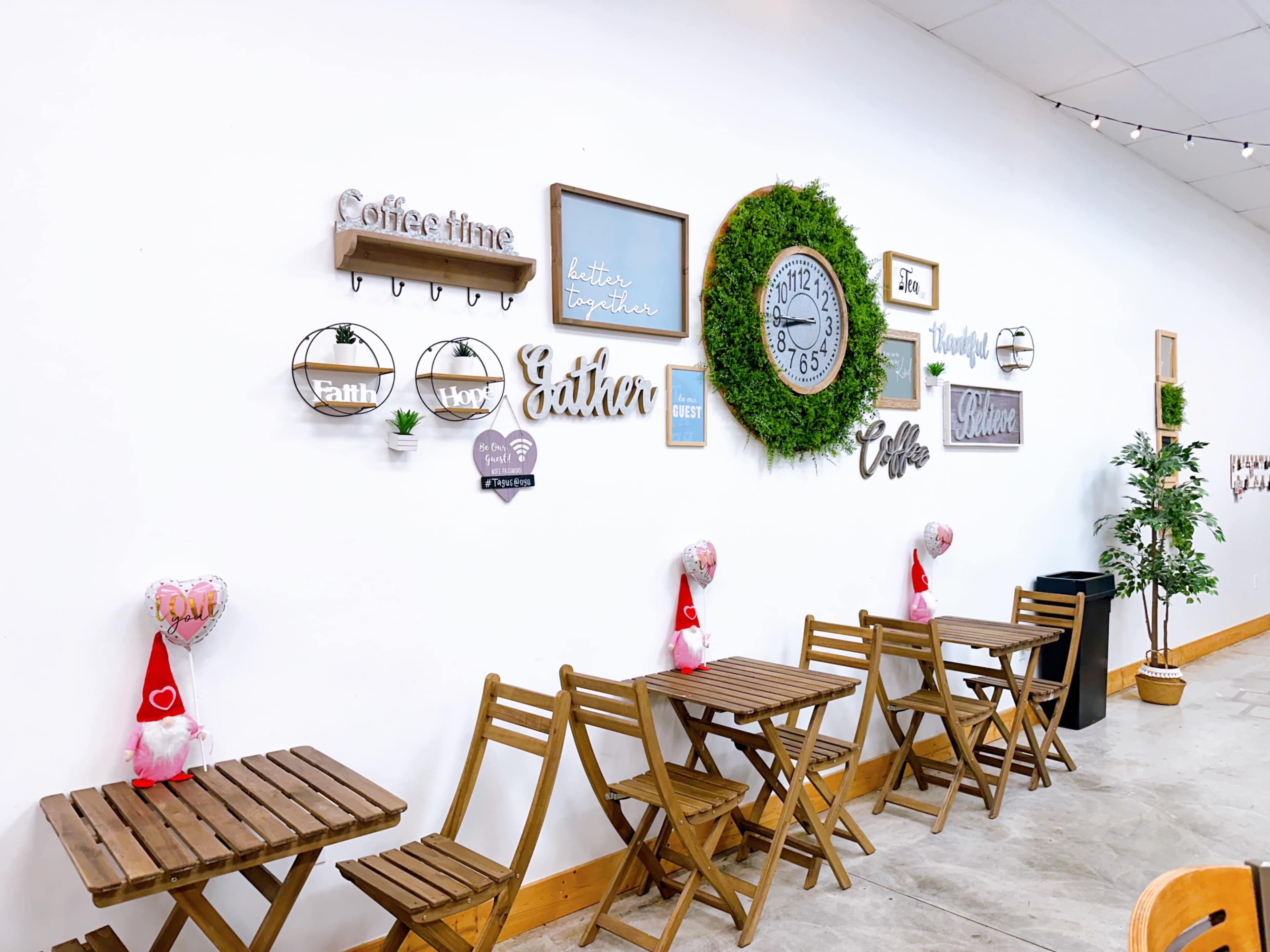 The image shows a cozy café interior with wooden tables and various decorative wall elements, including signs, a clock, and greenery.