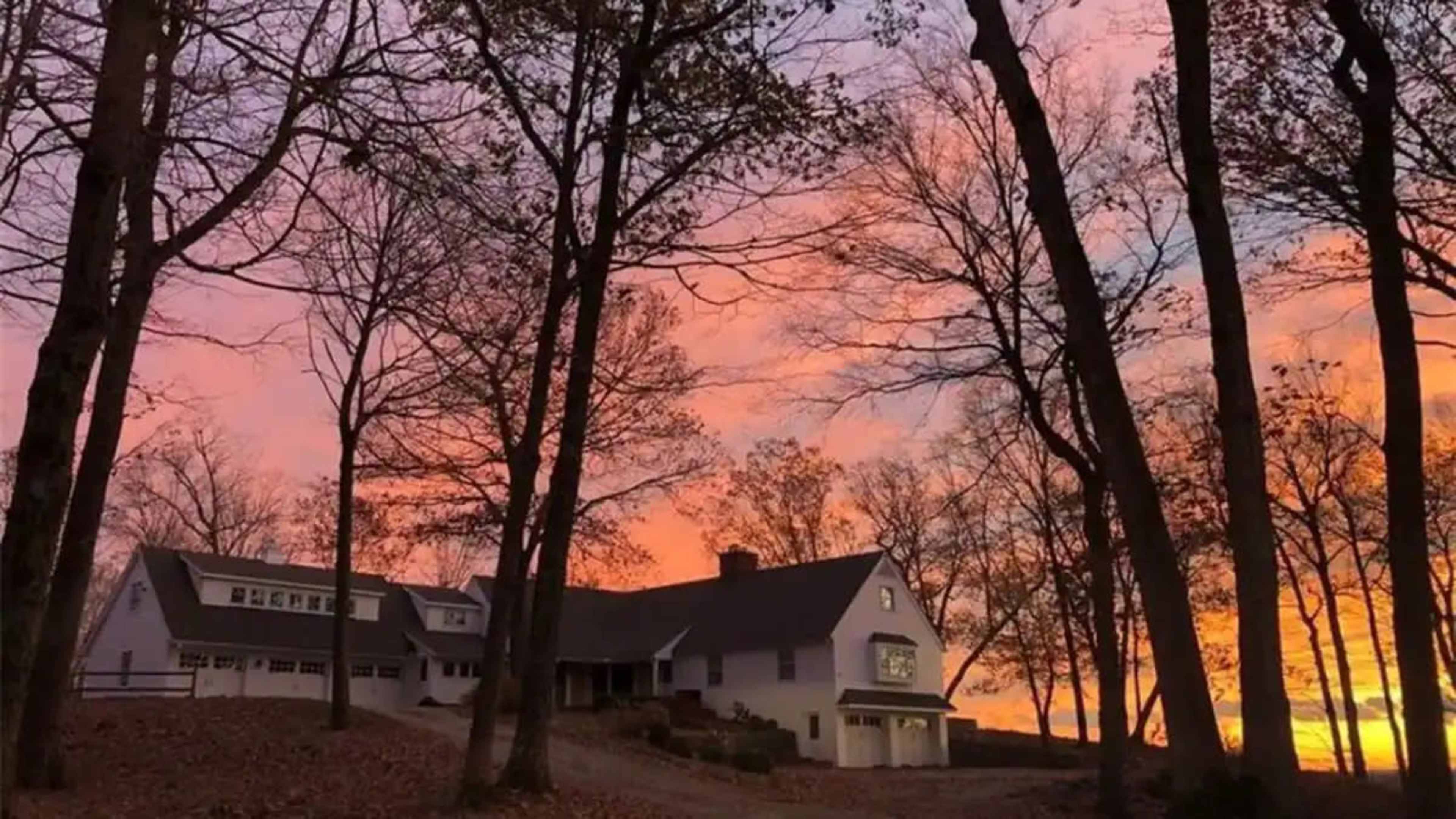 A house is framed by bare trees against a vibrant sunset sky.
