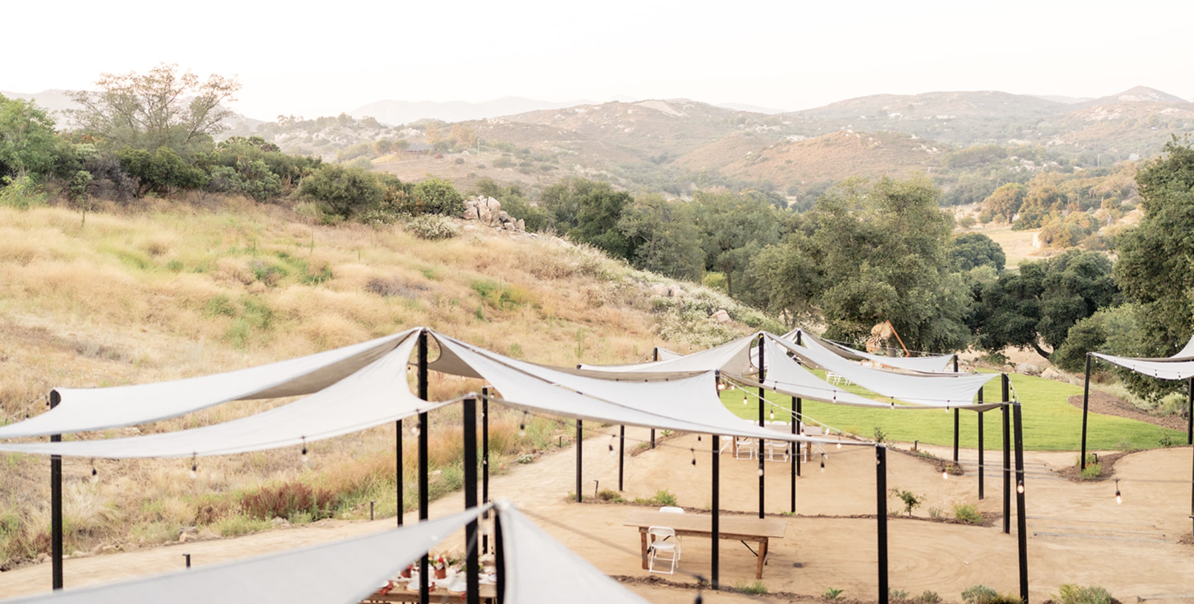 The image shows a landscape with several shaded structures in the foreground, overlooking rolling hills and a grassy area in the background.