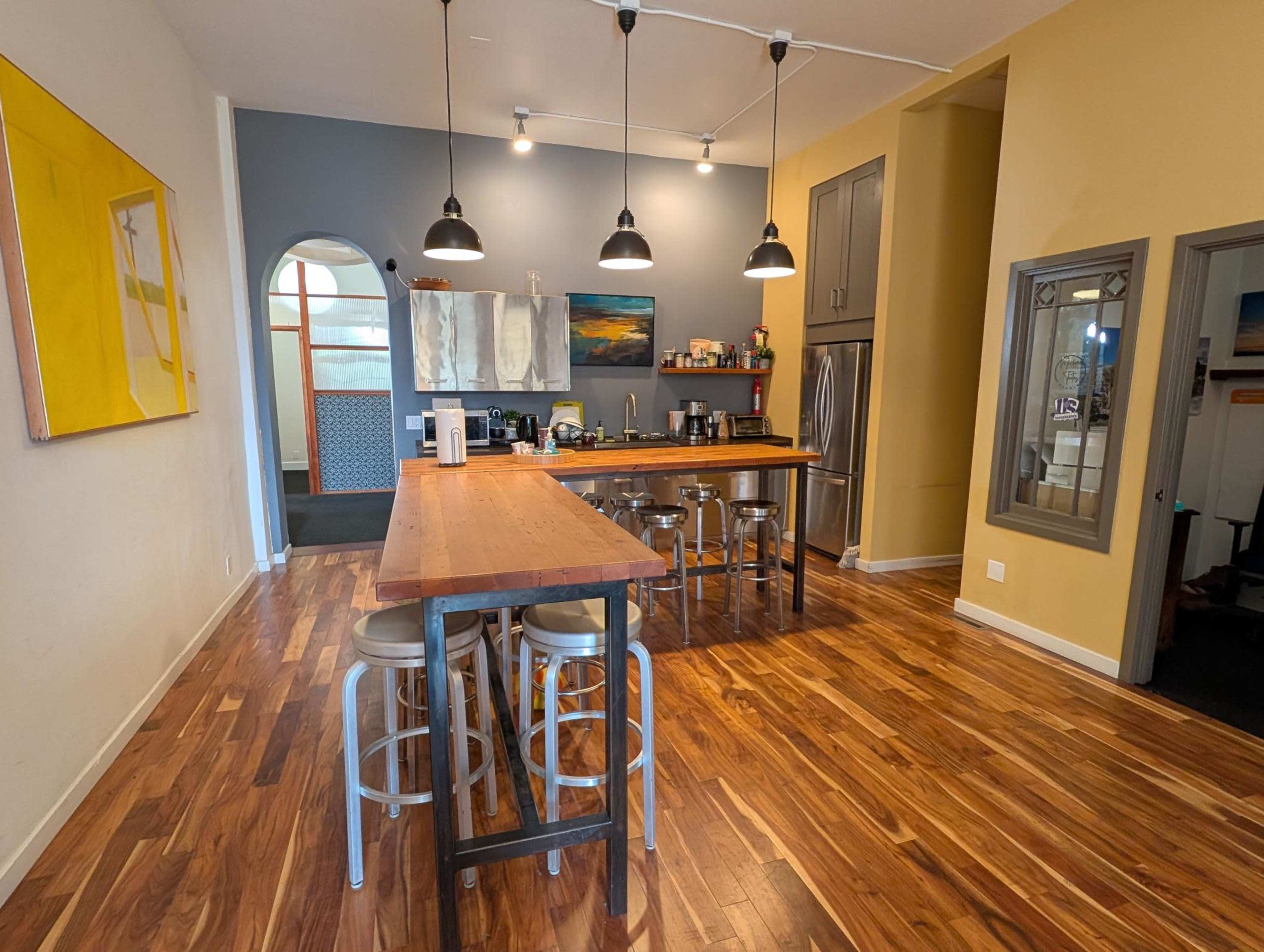 A modern kitchen features a wooden island with metal stools, stainless steel appliances, and a mix of yellow and gray walls.
