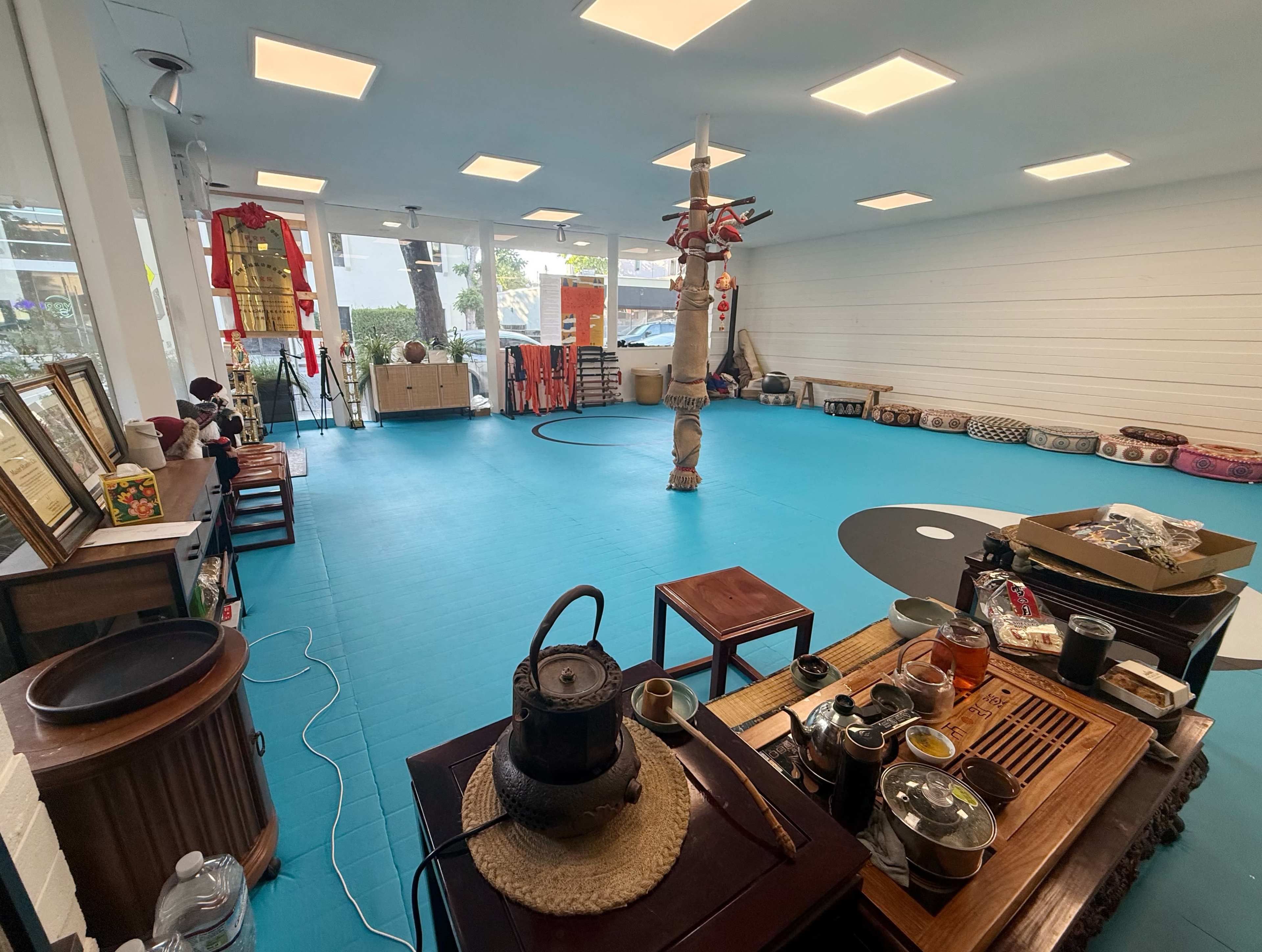 The image shows an empty room with a blue floor, featuring various furniture, decorations, and a tea setup along one side.