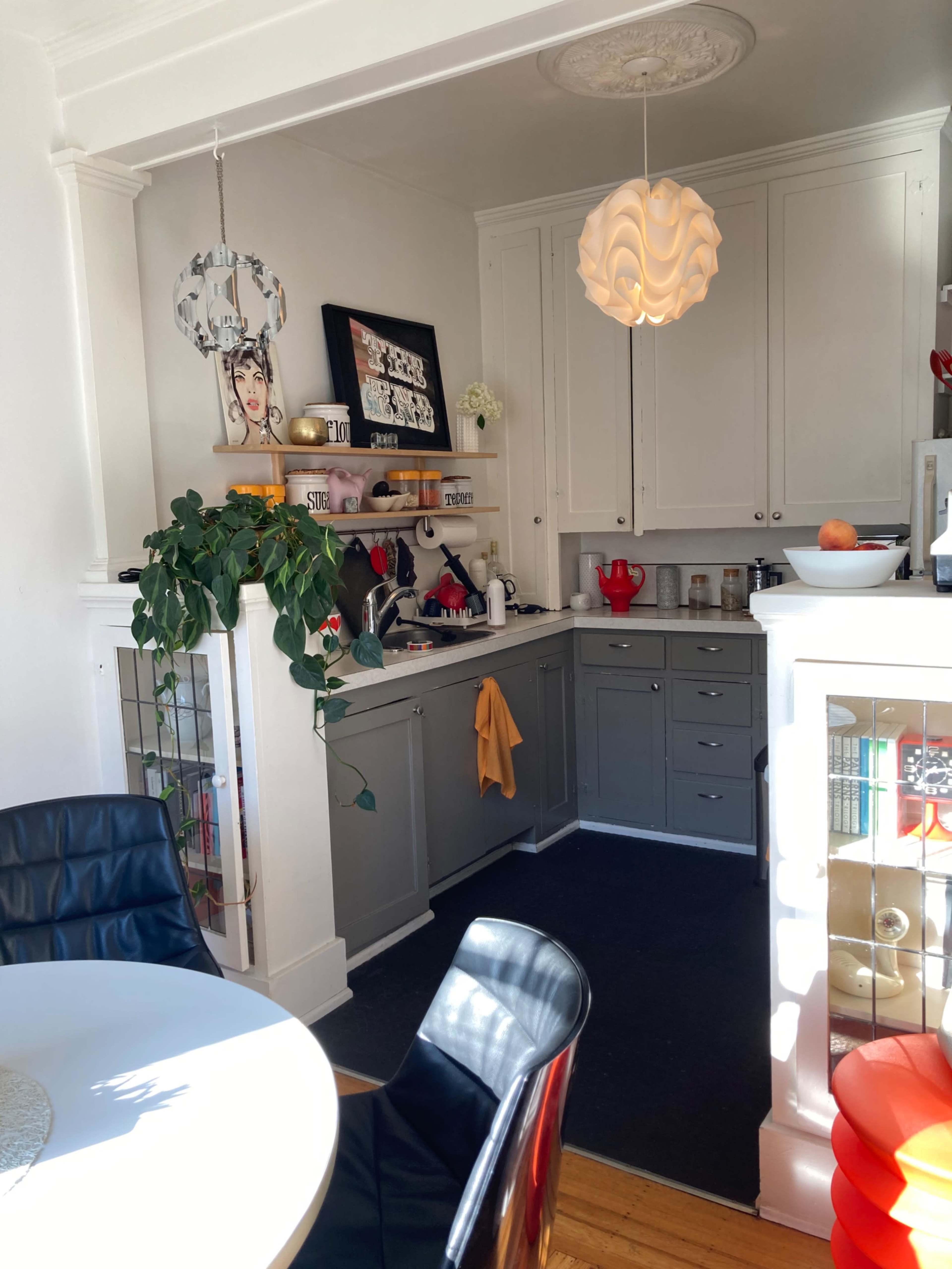 A modern kitchen with gray cabinets, a round dining table, and a hanging light fixture, featuring various kitchen items and decor on the counters and shelves.