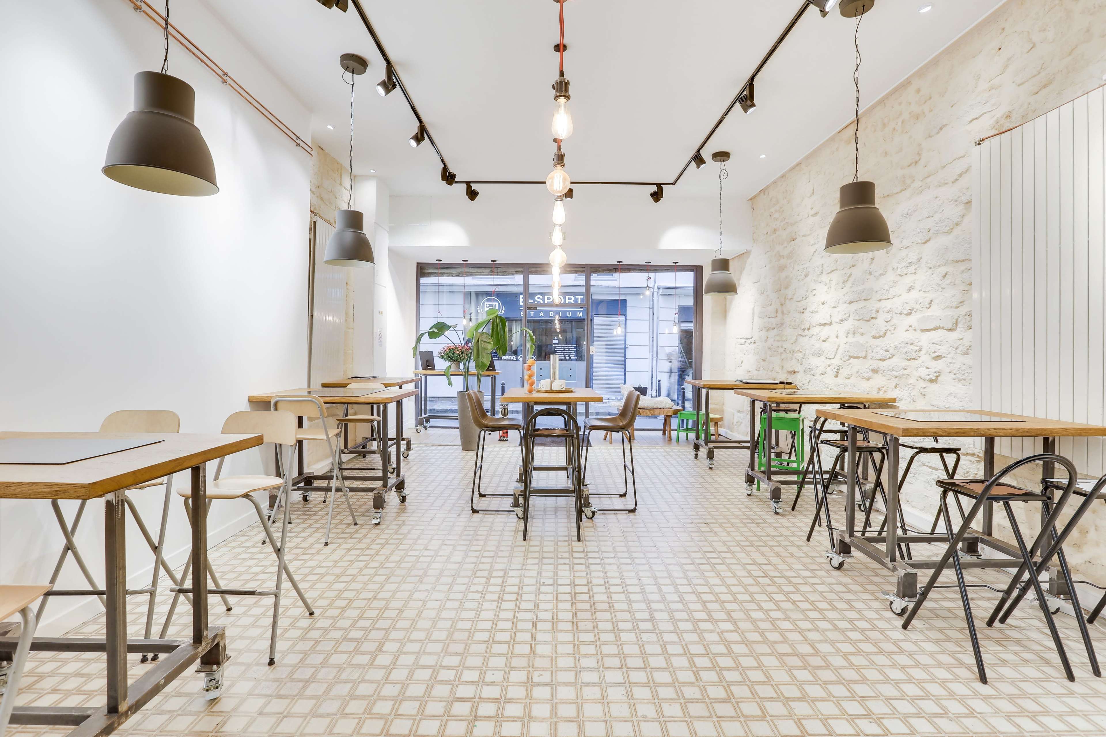 A modern café interior with wooden tables and metal chairs, featuring a tiled floor and pendant lighting.