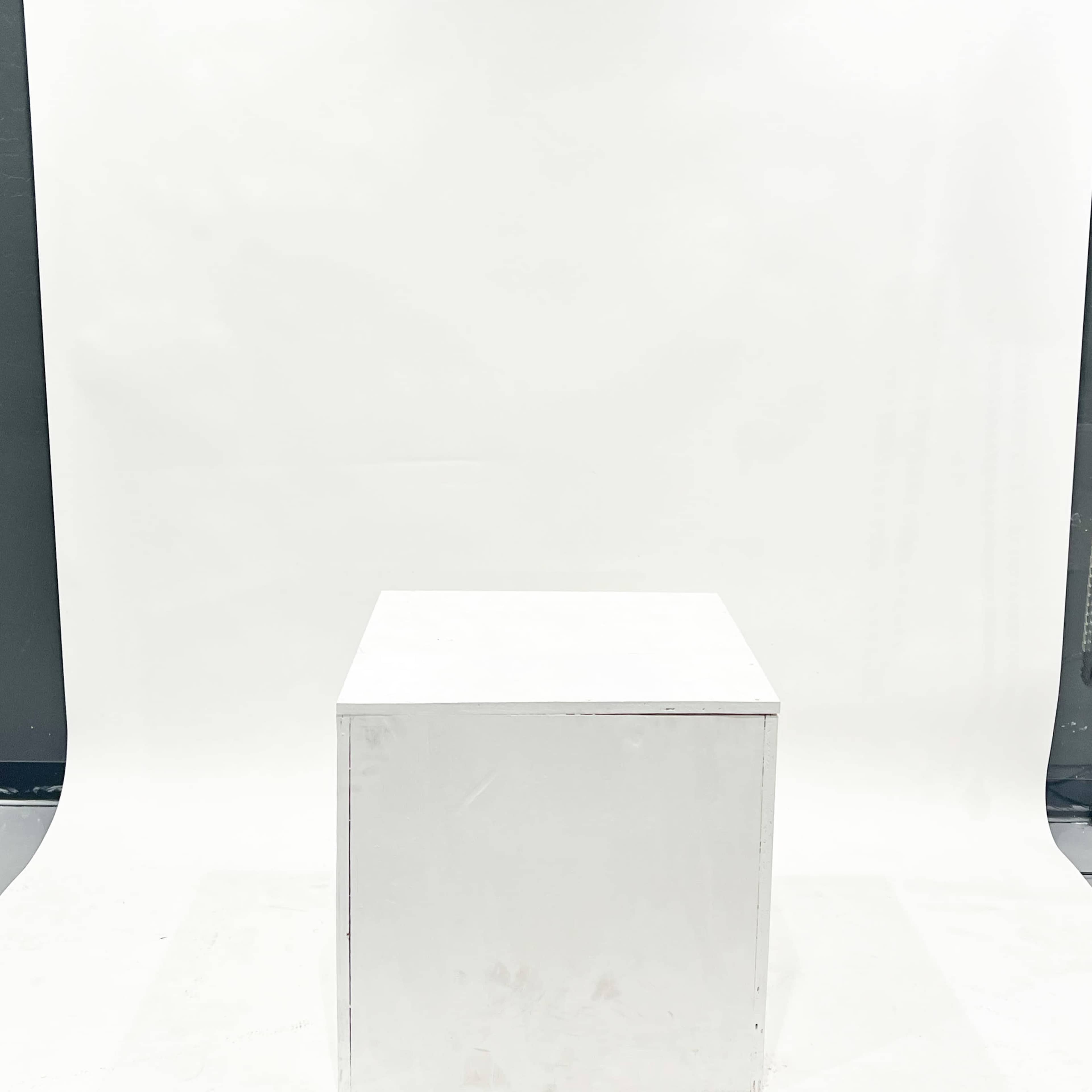 A plain white cube sits in the center of a studio space with a blank white backdrop.