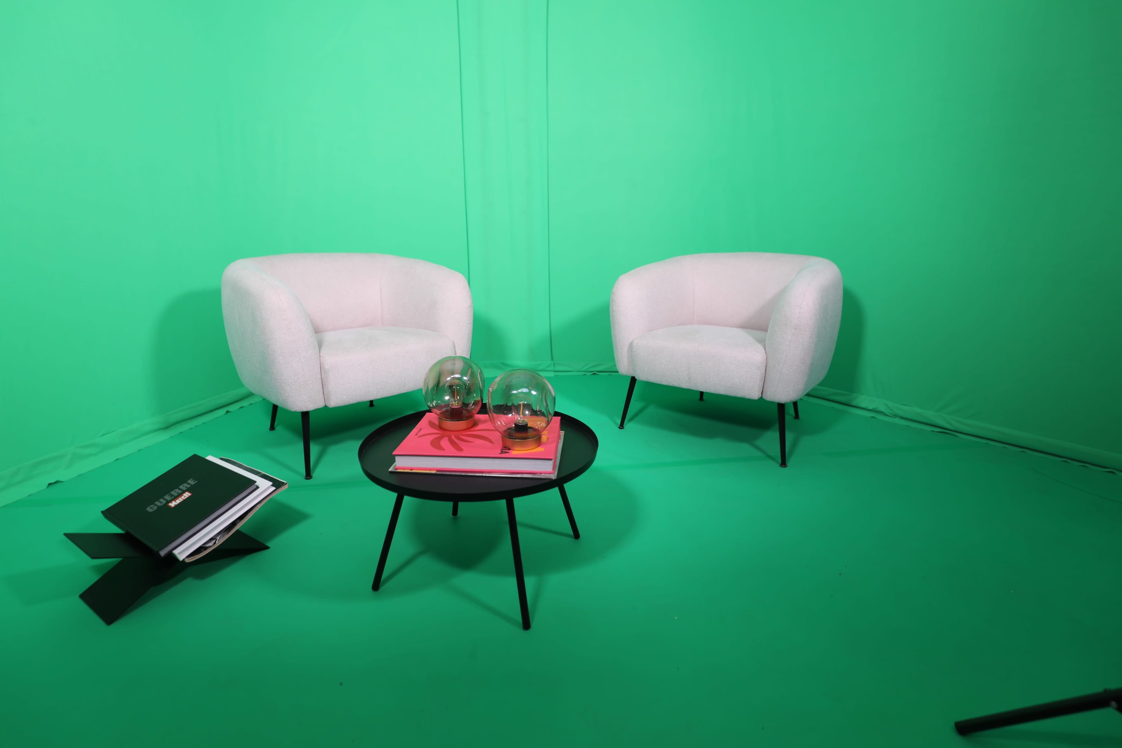 The image shows two white chairs and a round black coffee table with decorative items, all set against a bright green backdrop.