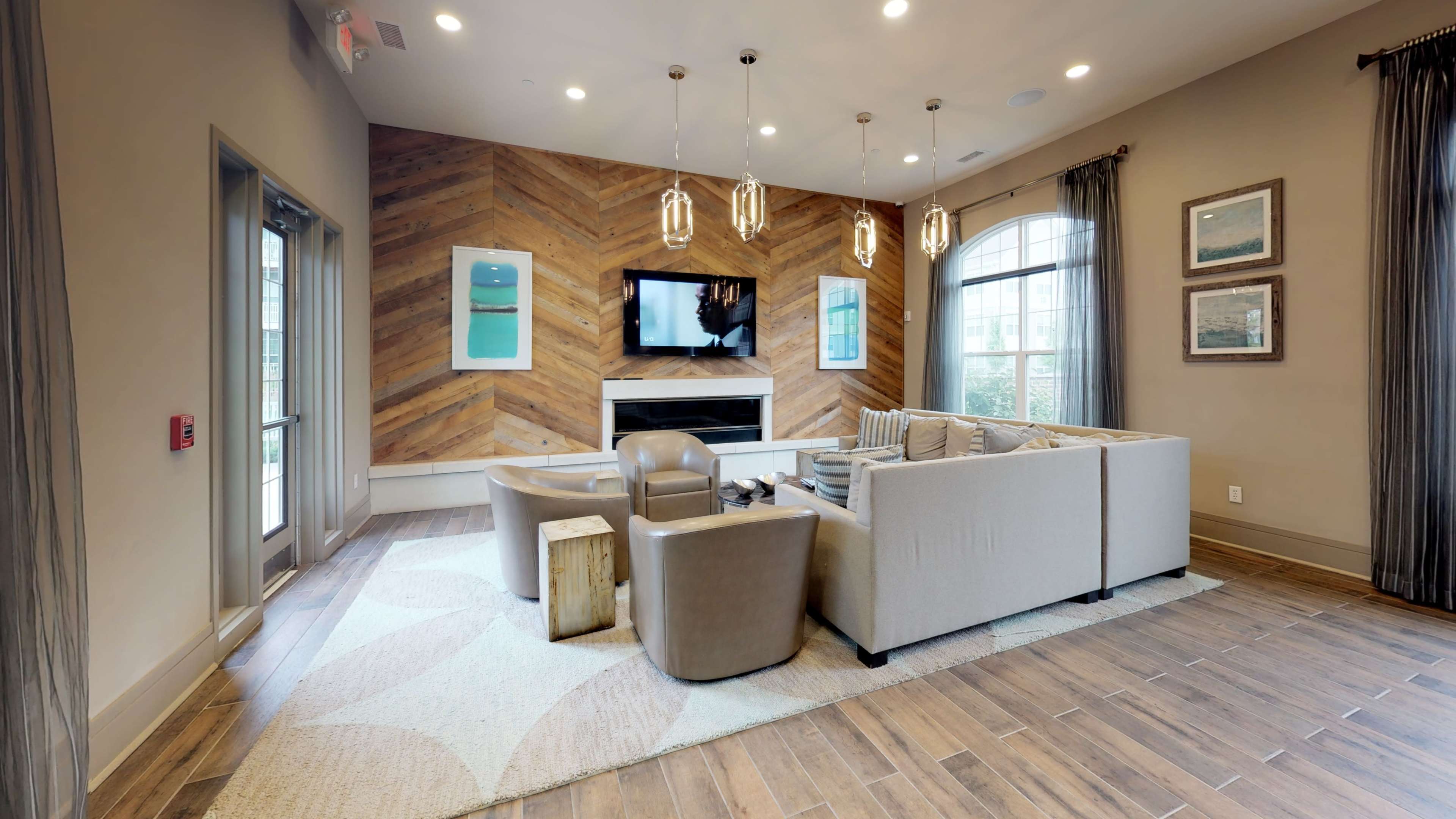 A modern lounge area features a sectional sofa, armchairs, and a television mounted on a wooden accent wall.