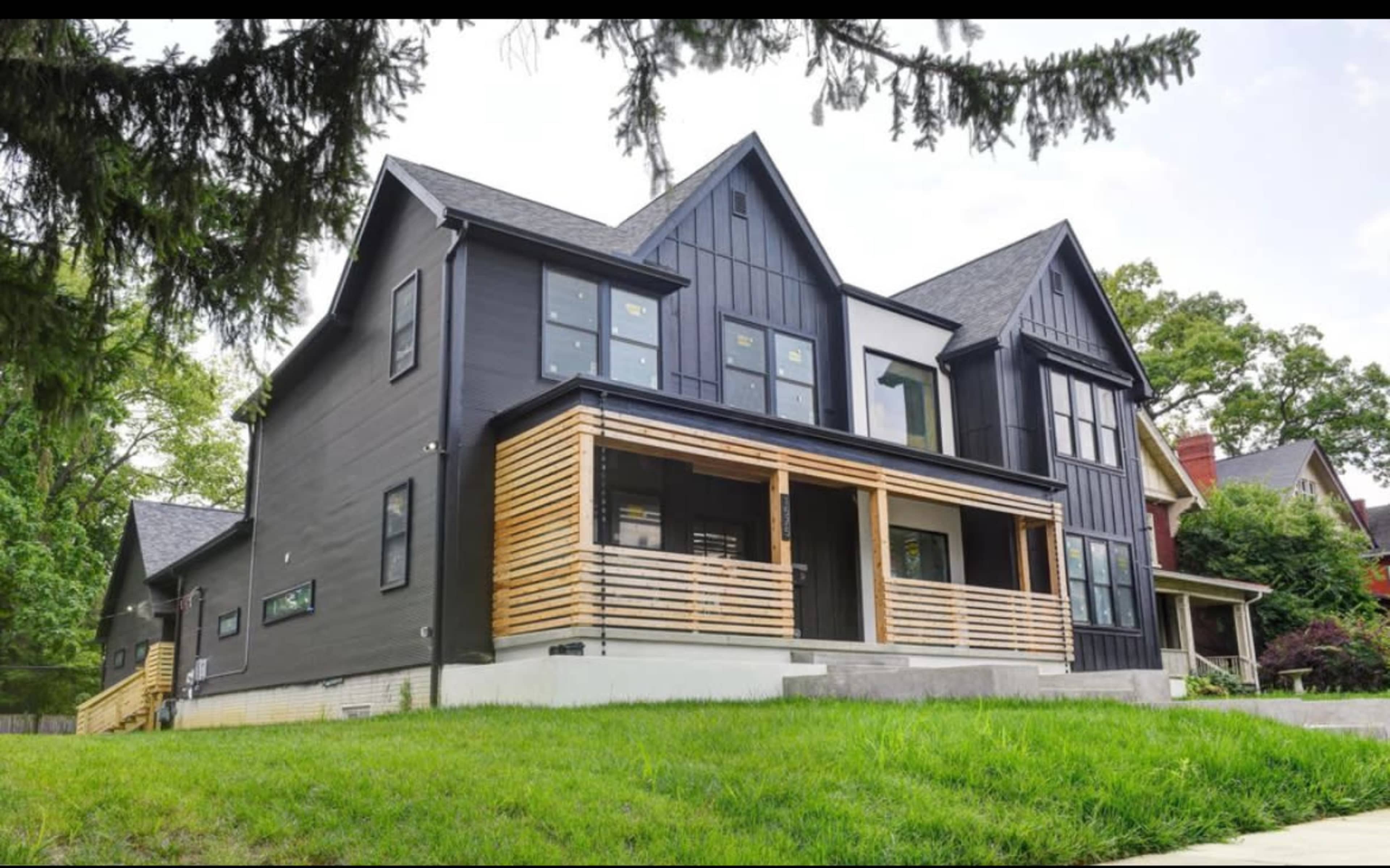 A modern black house with wooden accents and a front porch is surrounded by a green lawn.