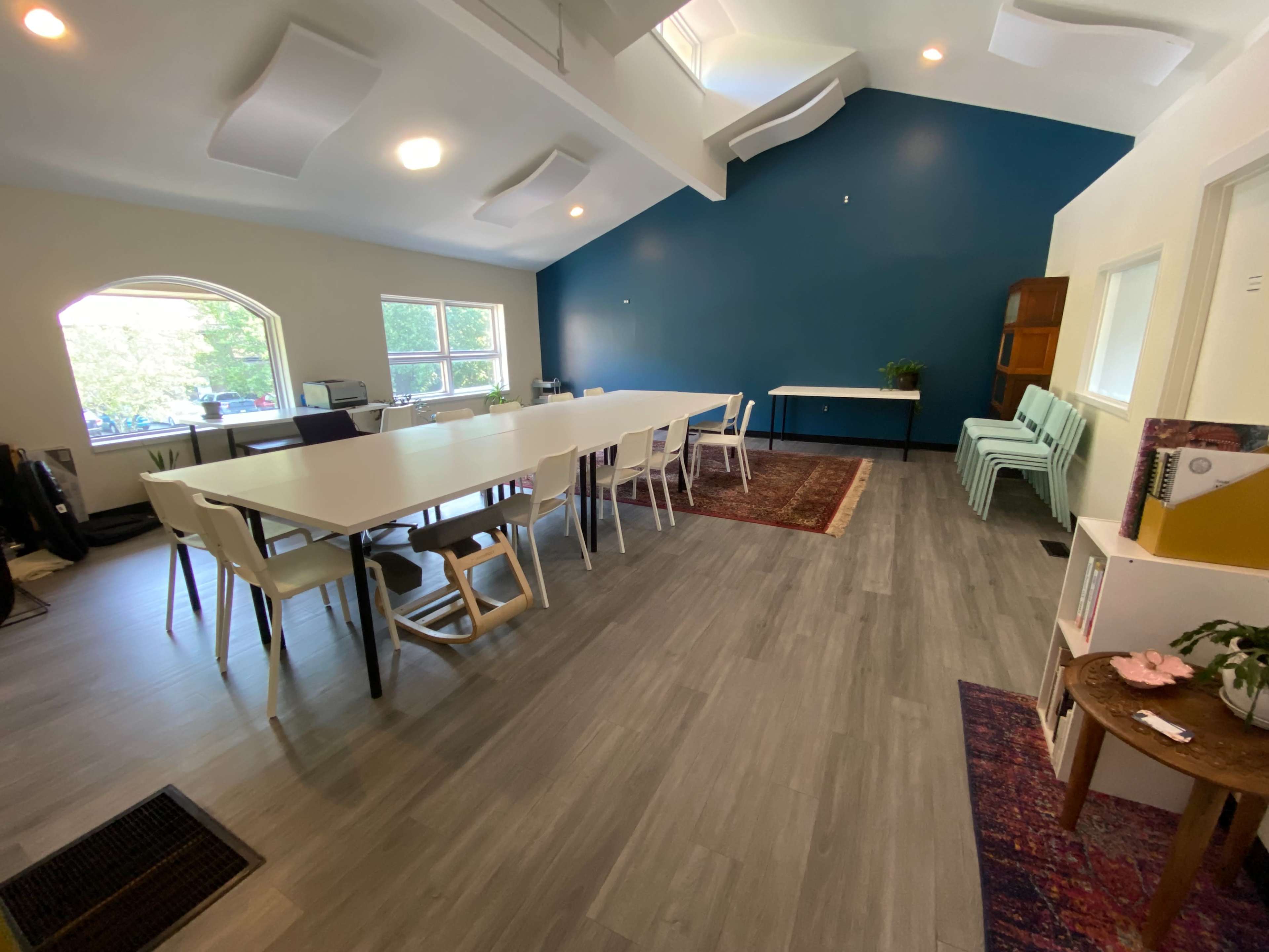The image shows a bright, spacious meeting room with a long white table, light green chairs, and blue accent wall.