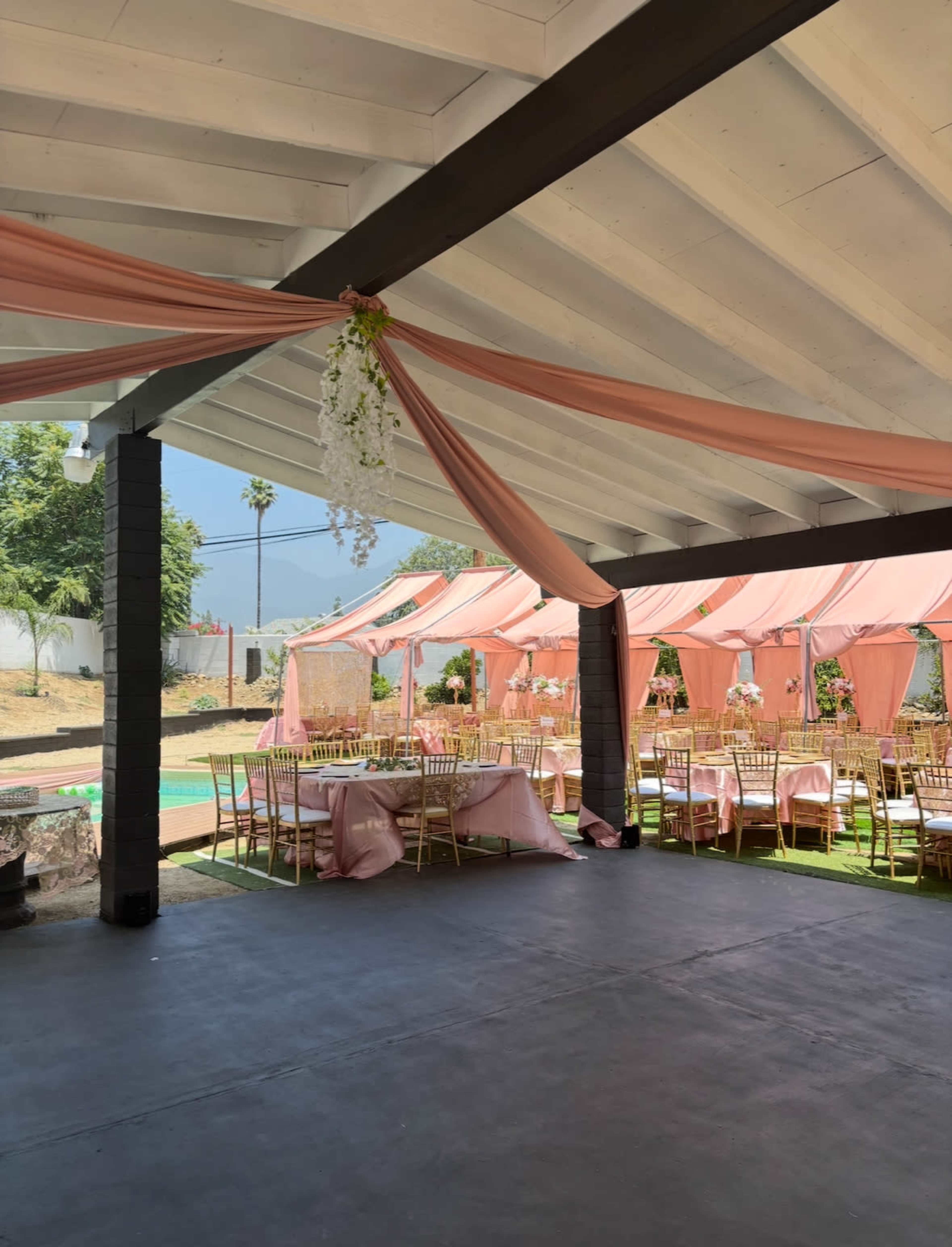 The image shows a decorated outdoor event space with pink drapery and tables set for a celebration.