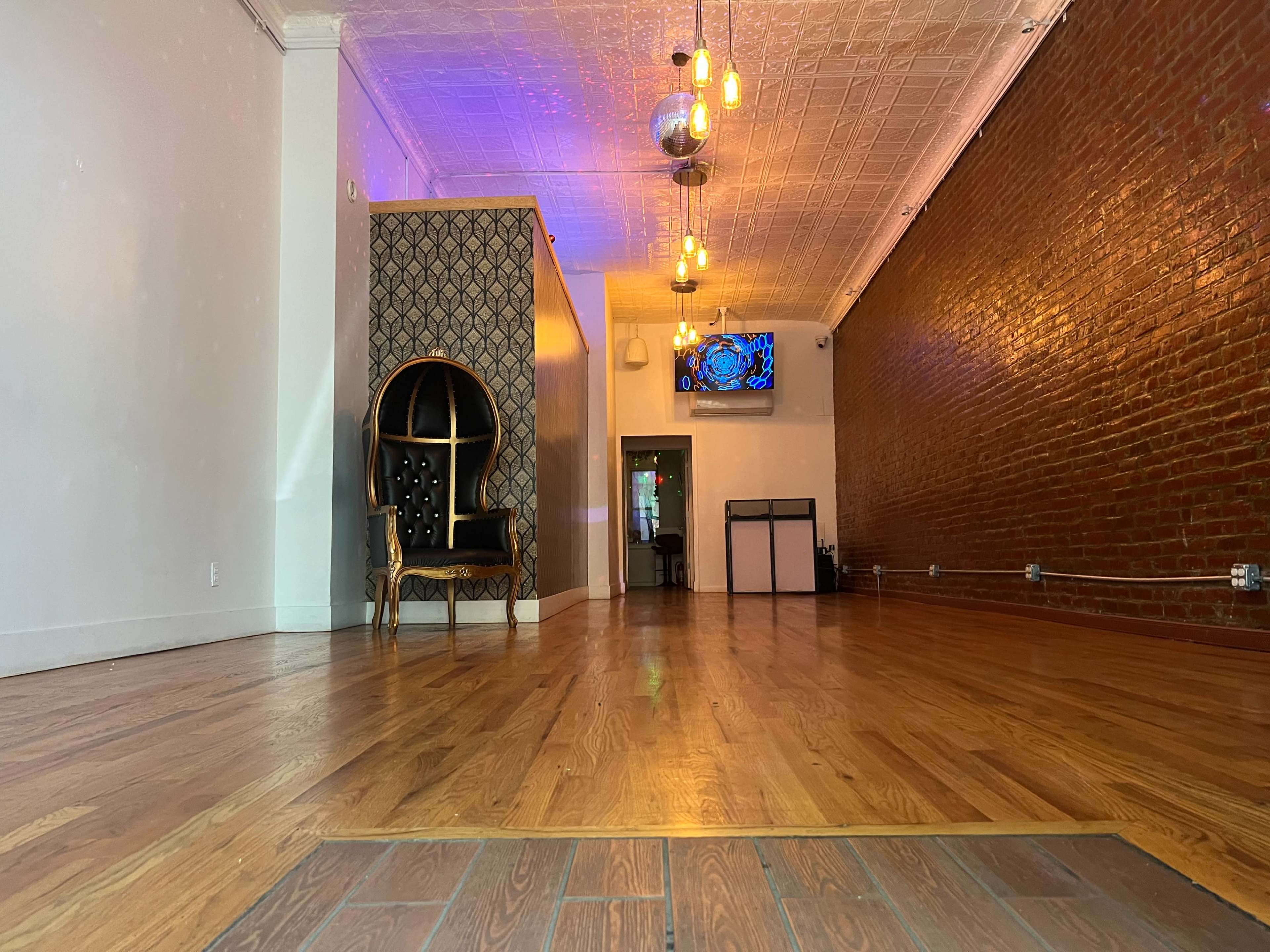 An empty interior space with wooden floors, a decorative chair, and a wall-mounted television in a well-lit area.