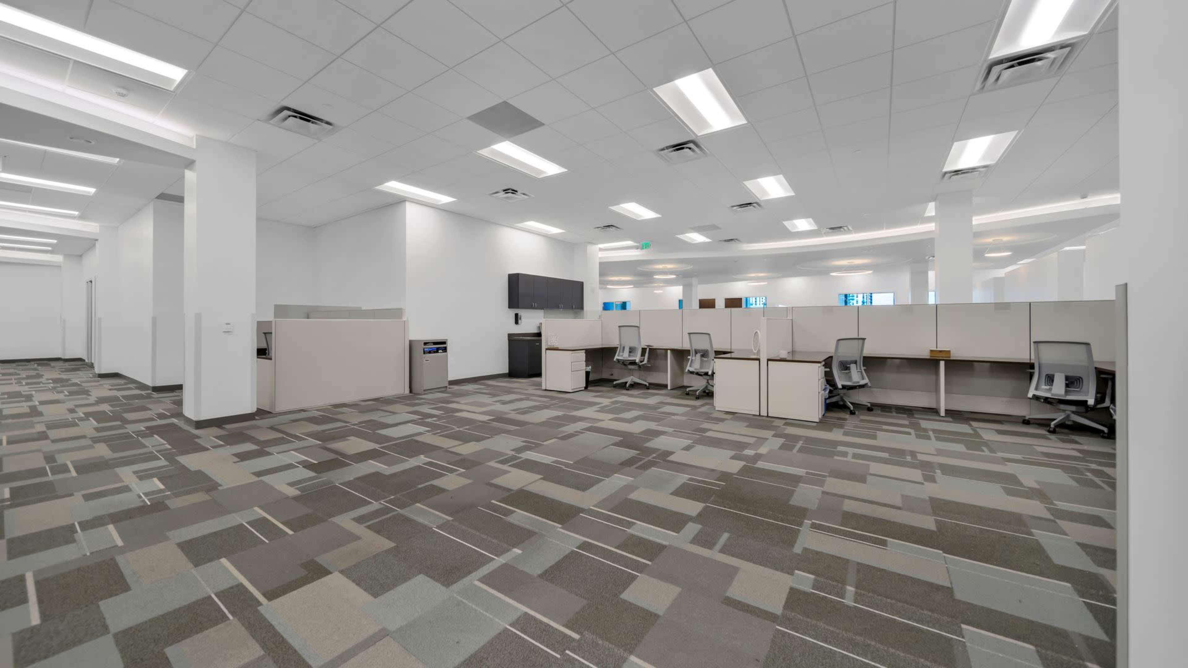 A spacious, empty office area with cubicles, modern furnishings, and a patterned carpet.
