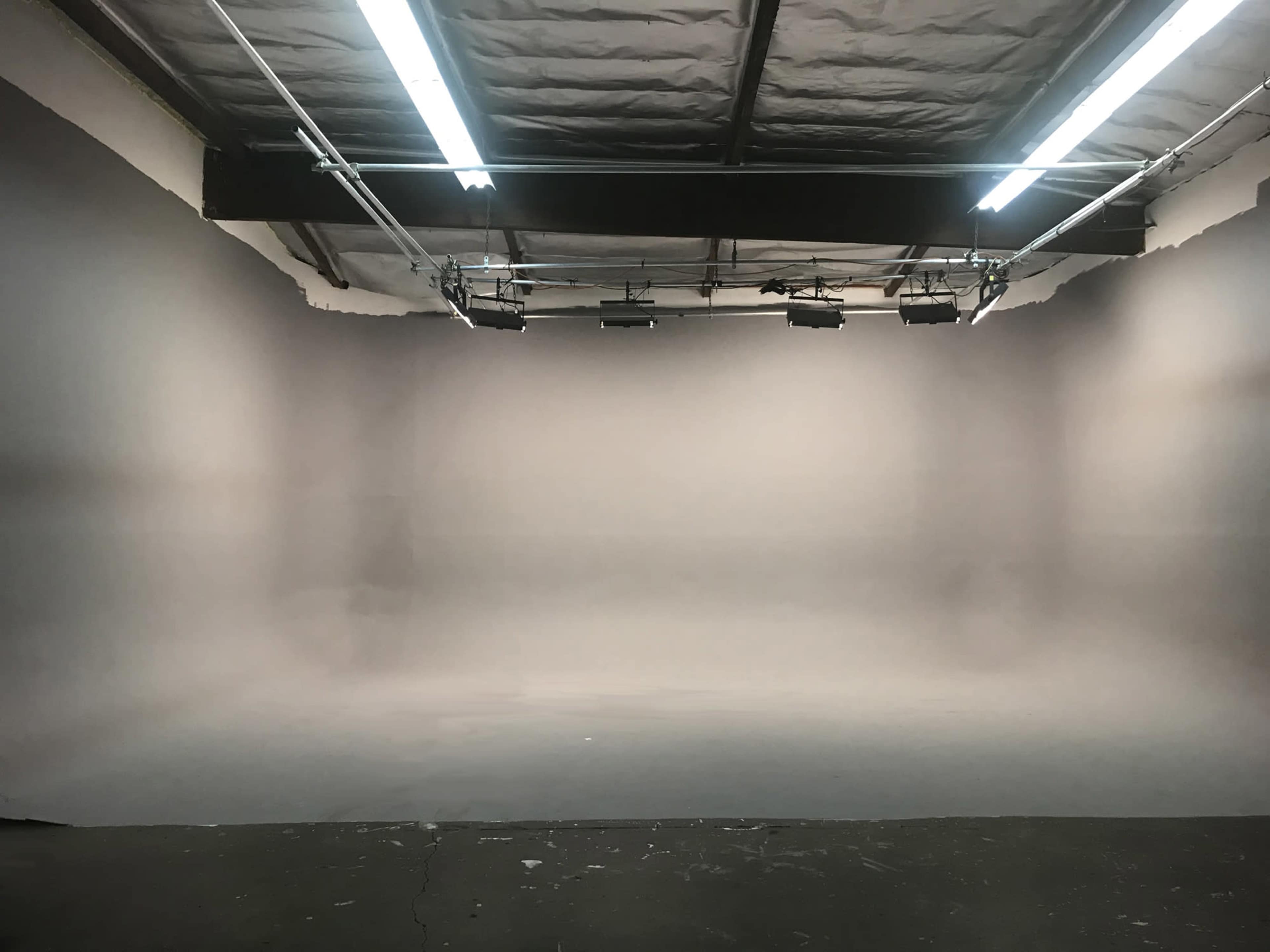 An empty photography studio with gray walls and overhead lighting.