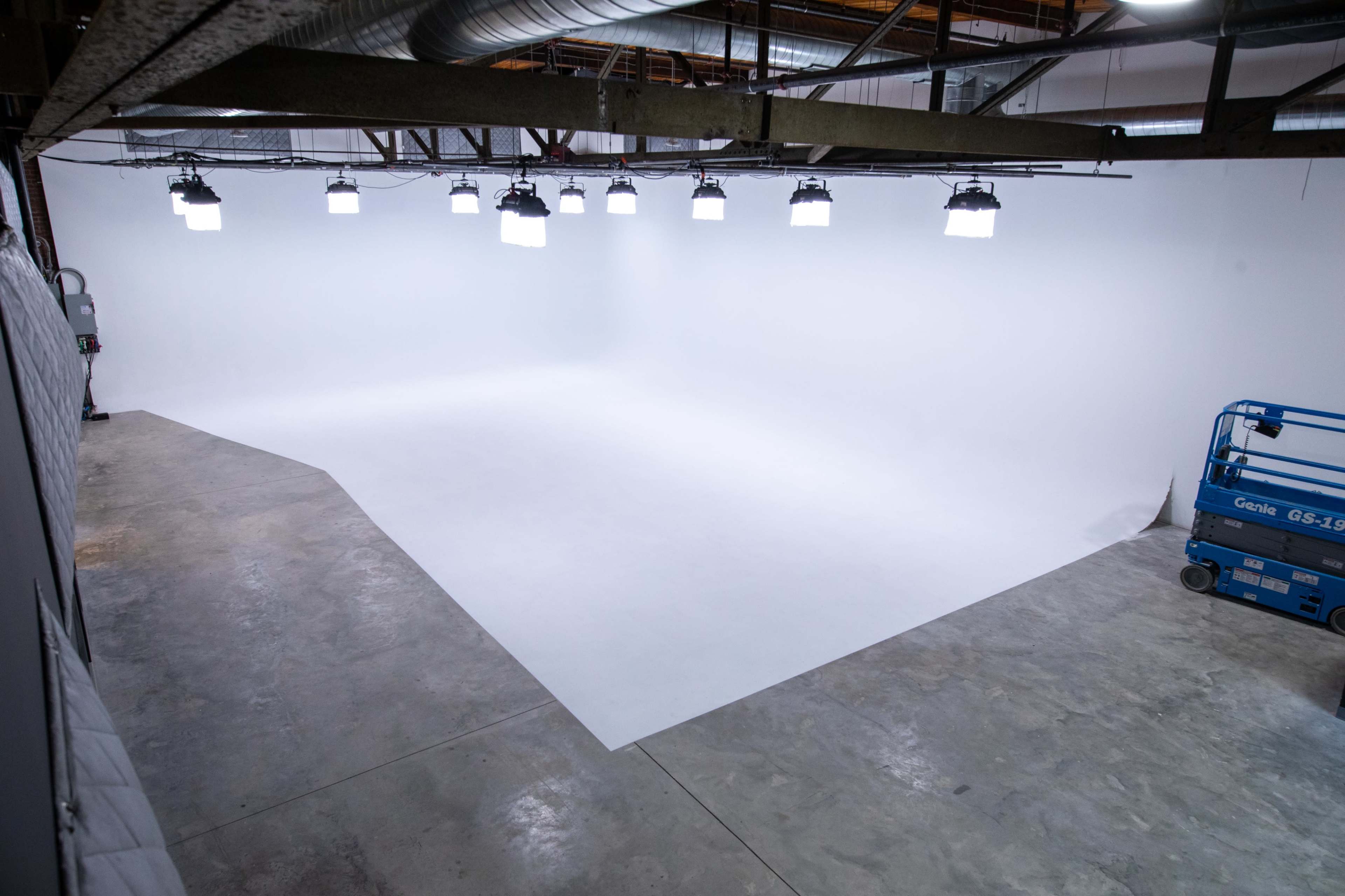 A spacious, well-lit studio with a seamless white backdrop and a blue scissor lift in the corner.