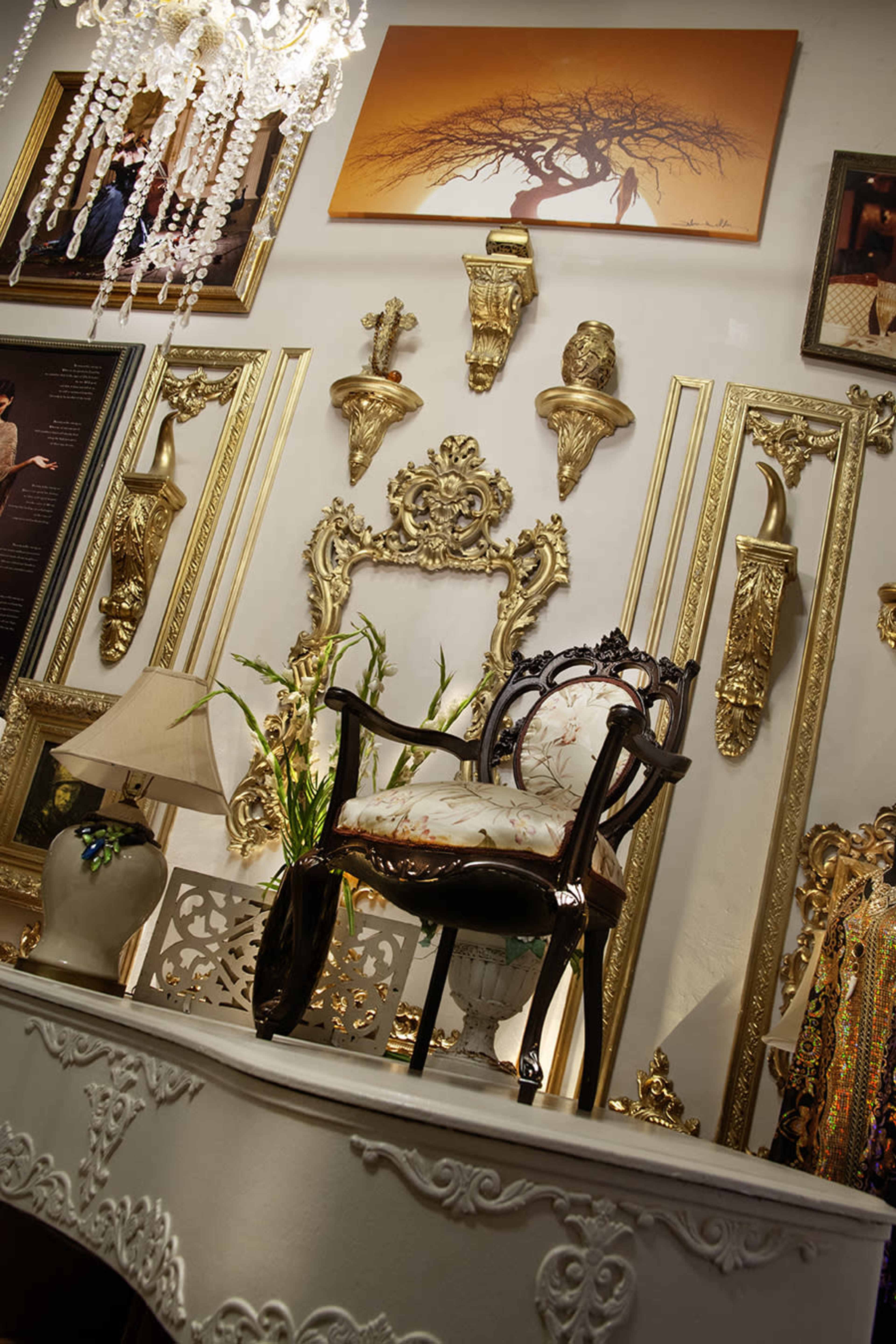 The image features an ornate display with a decorative chair on a table surrounded by framed artwork and intricate wall decorations.