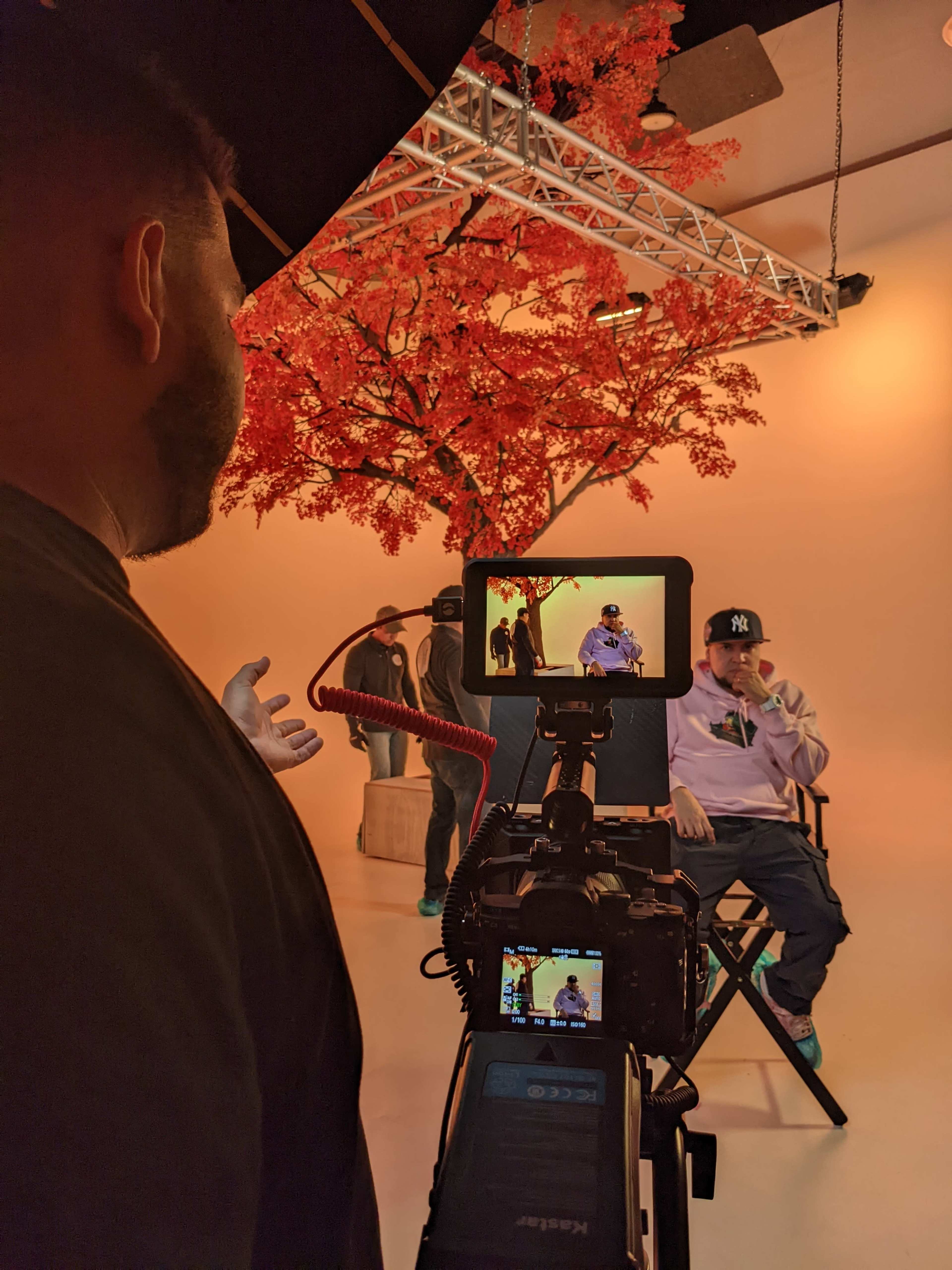 A photographer captures an individual seated in front of a large artificial tree in a studio setting.
