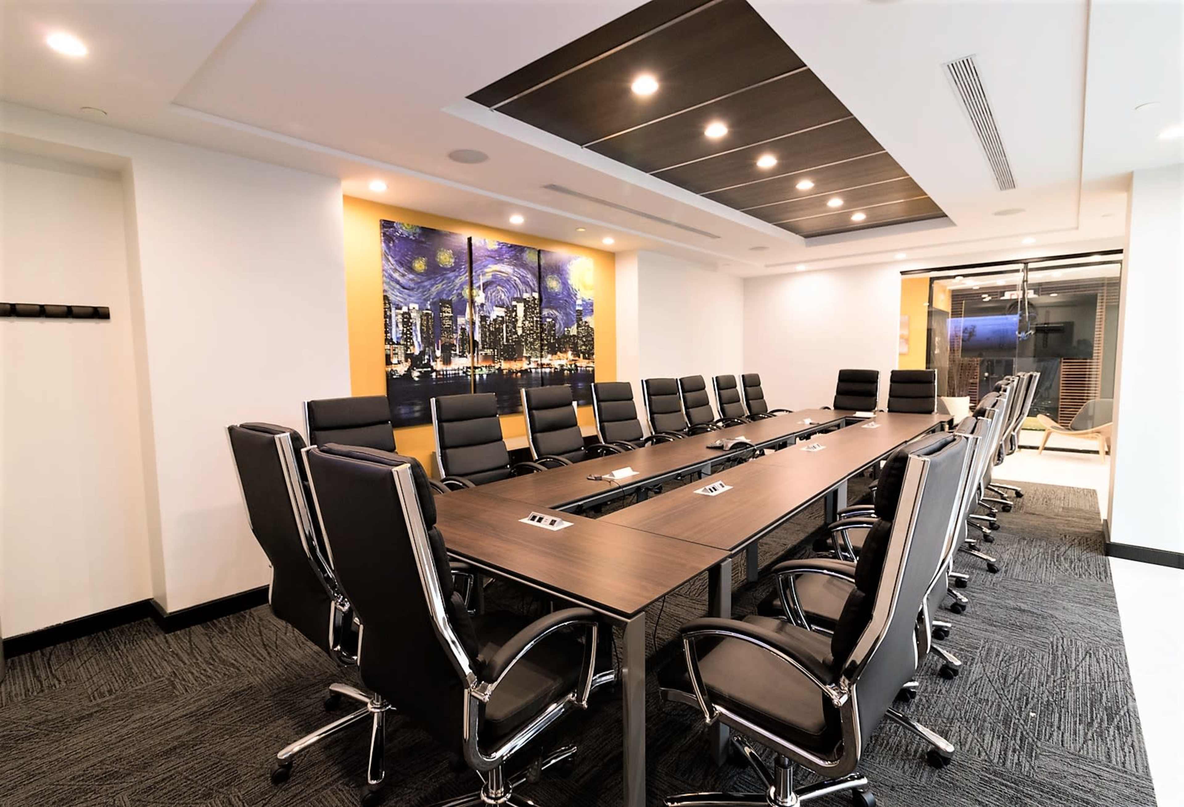 A modern conference room features a large rectangular table surrounded by black leather chairs, with a cityscape mural on one wall.