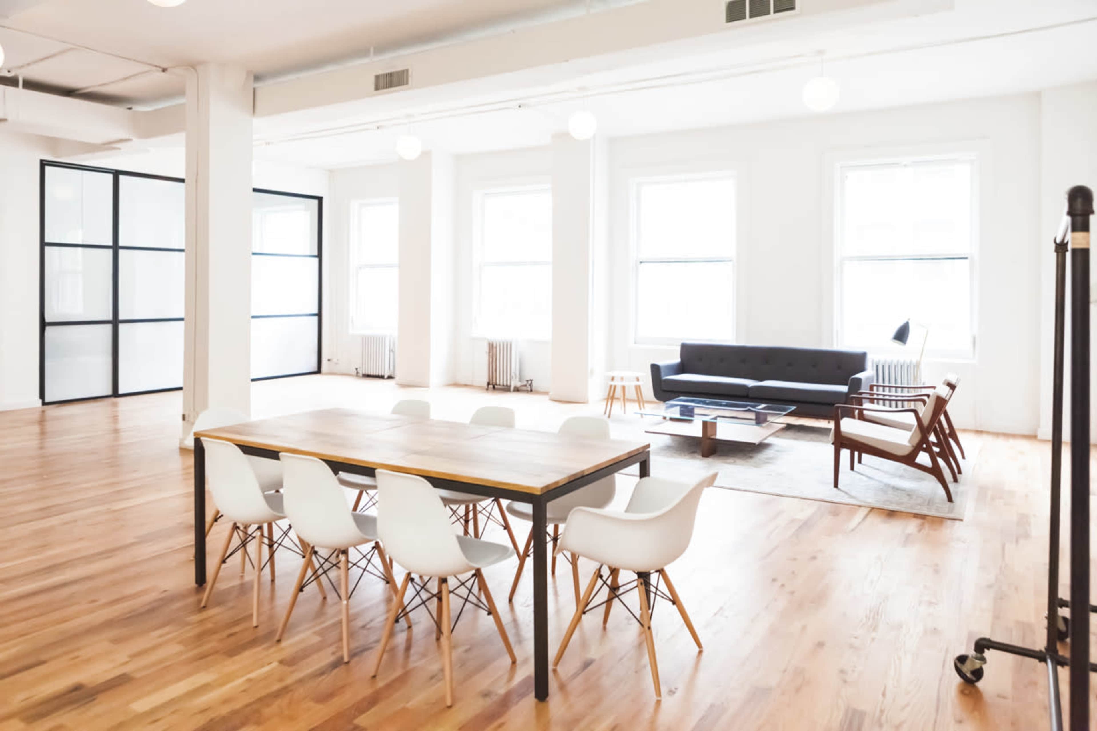 A spacious, modern room featuring a dining table with white chairs, a comfortable seating area with a dark sofa and armchairs, and large windows providing natural light.