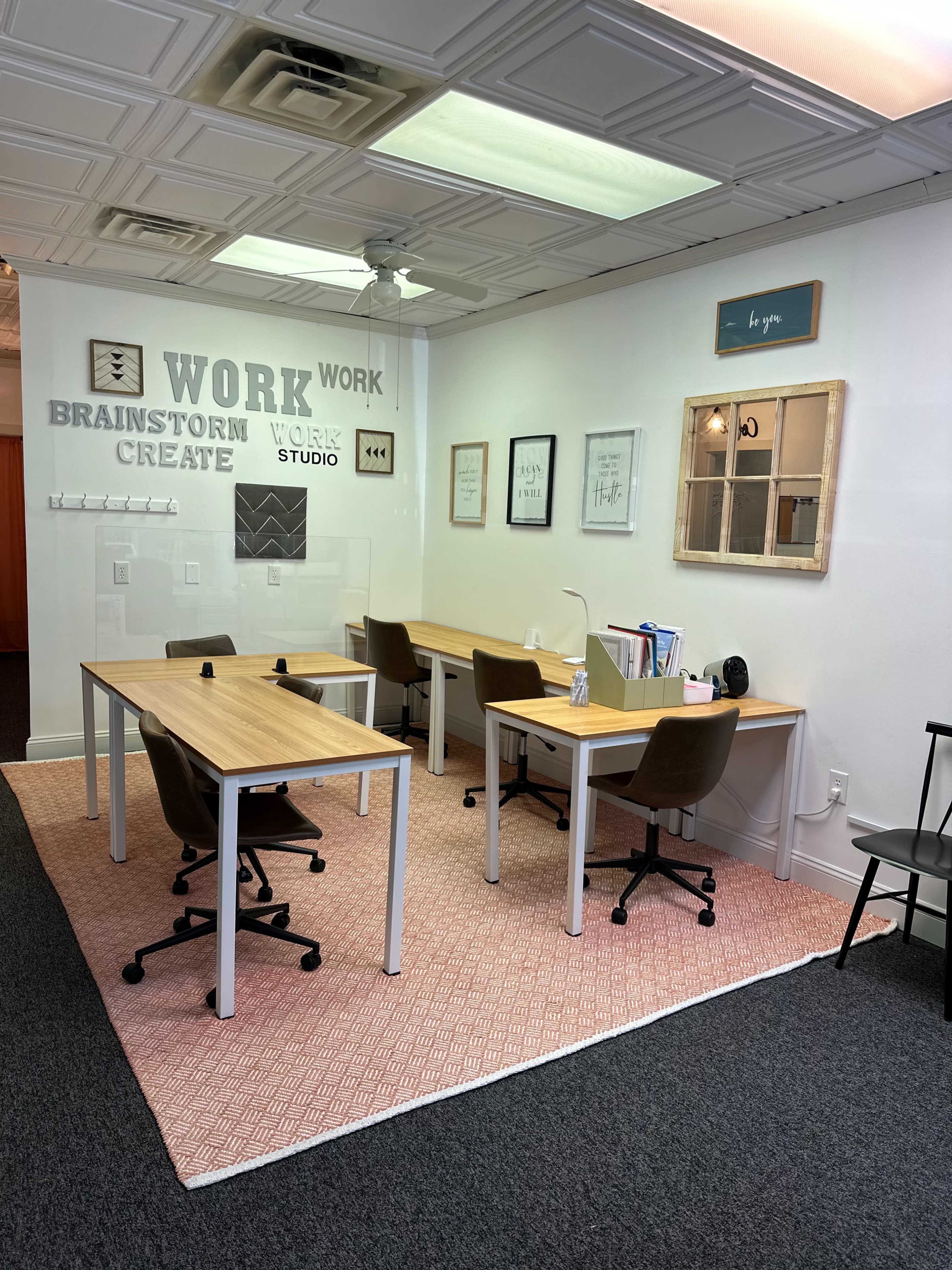A workspace with two wooden desks and chairs arranged on a patterned rug, complemented by wall art and a mirror.
