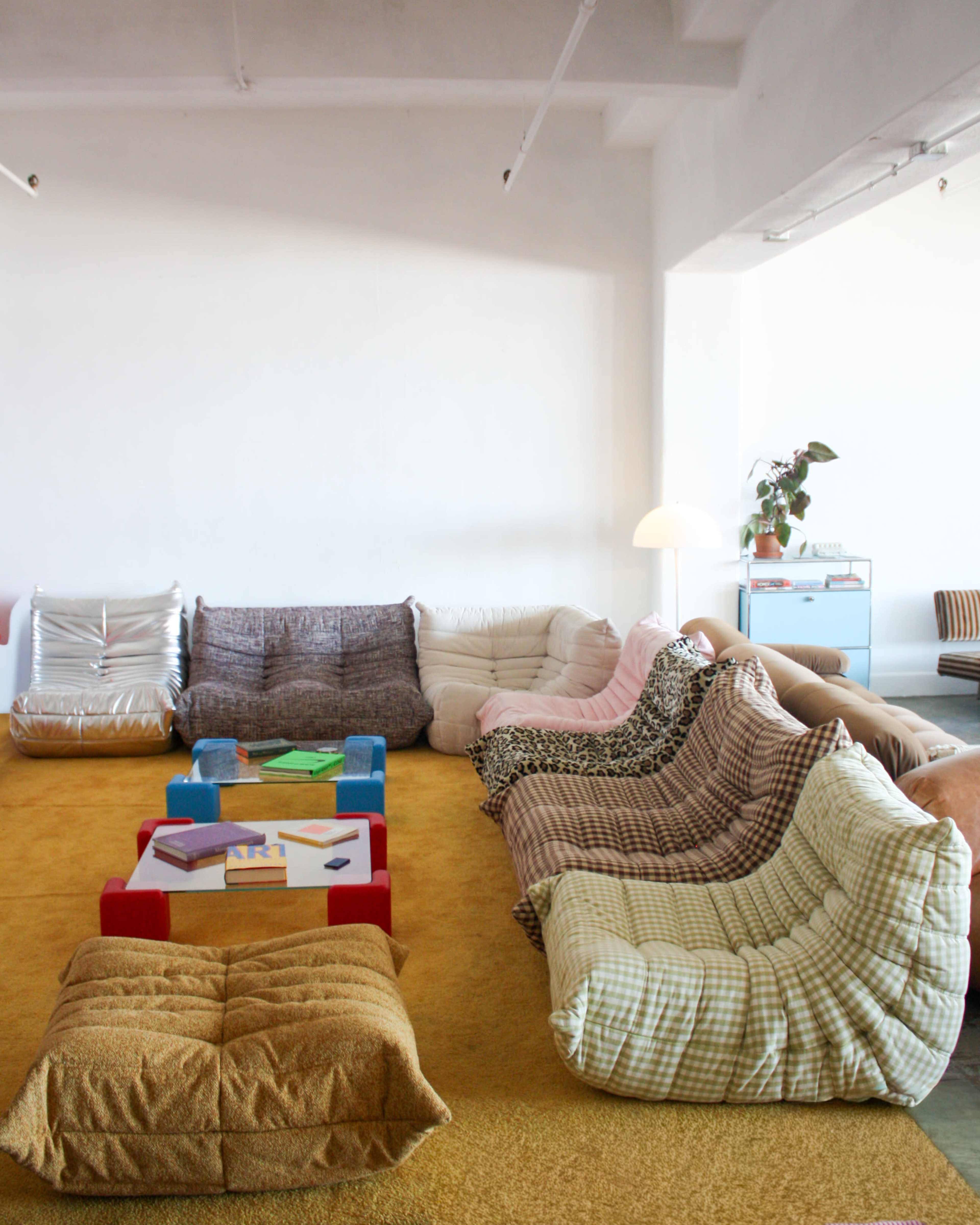 The scene features a cozy lounge area with several distinct patterned floor cushions arranged around a low, colorful coffee table on a carpeted surface.