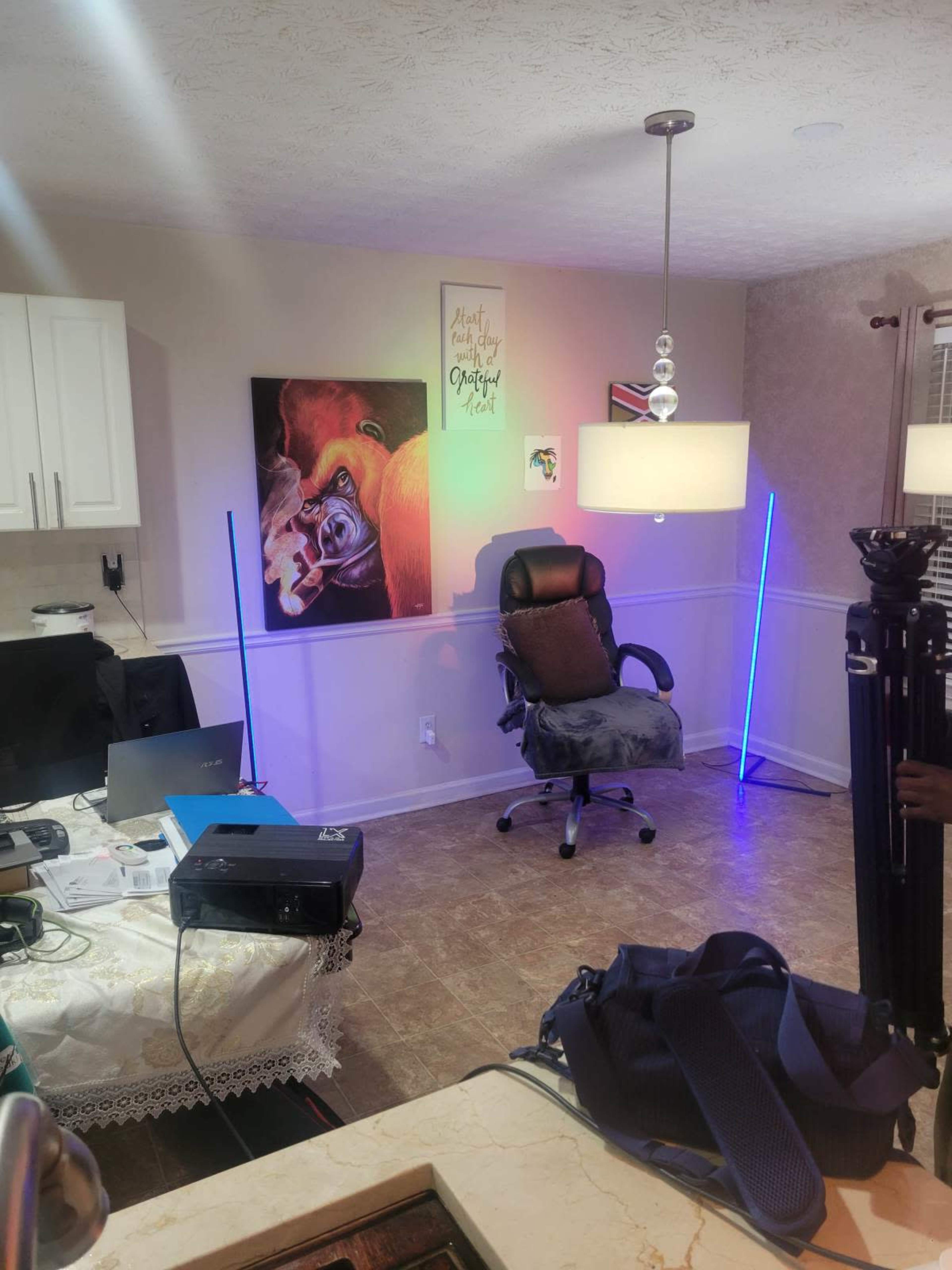 The image shows an indoor room with a chair, a table with a laptop and projector, and colored LED lights on either side of the chair.