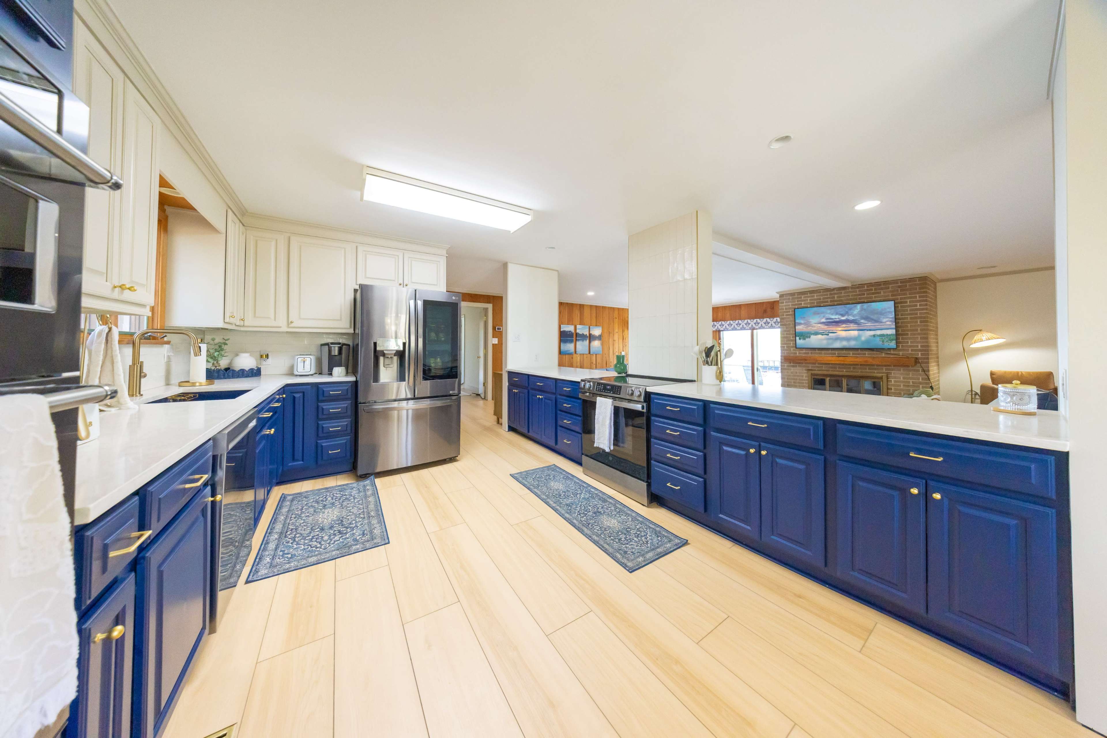 The image shows a spacious kitchen with blue cabinets, a stainless steel refrigerator, and a hardwood floor.