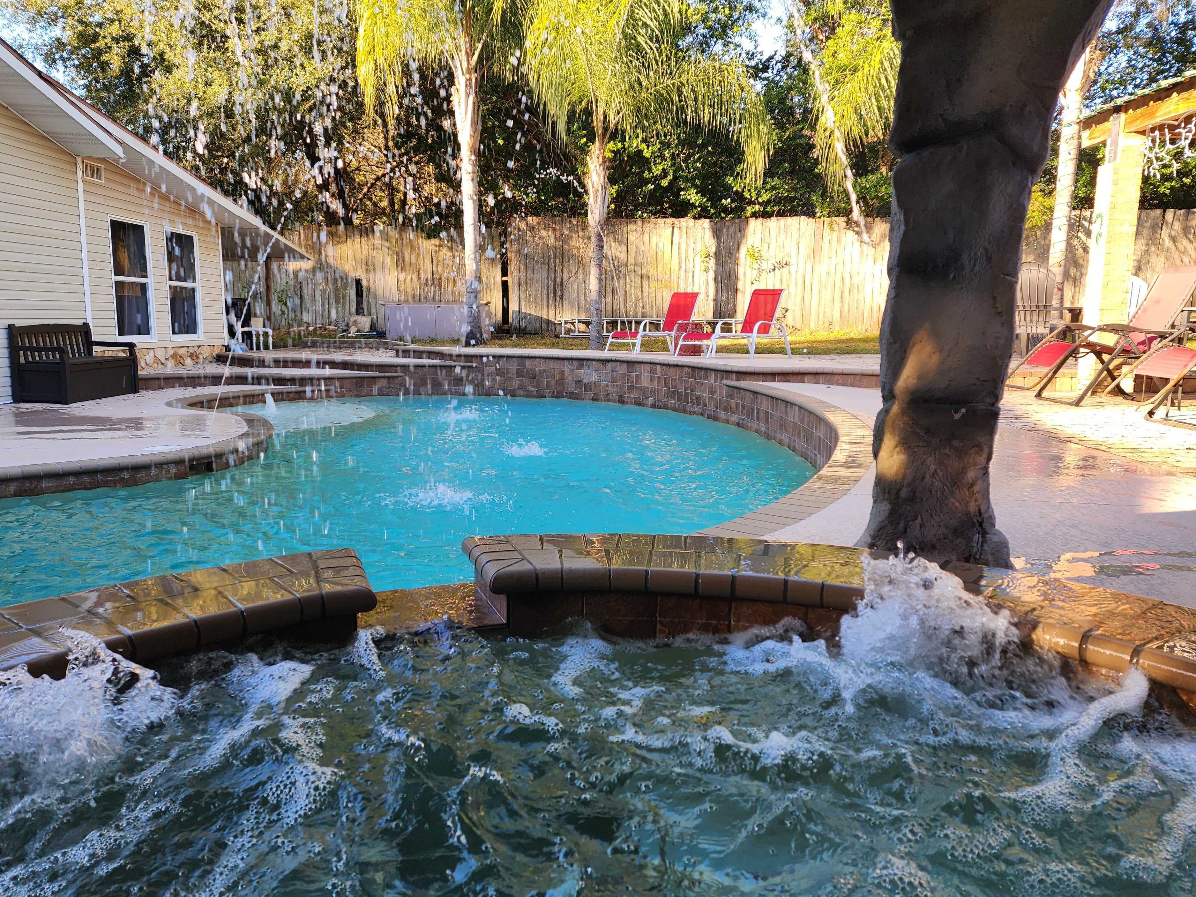 A swimming pool area with a waterfall feature, surrounded by palm trees and lounge chairs.