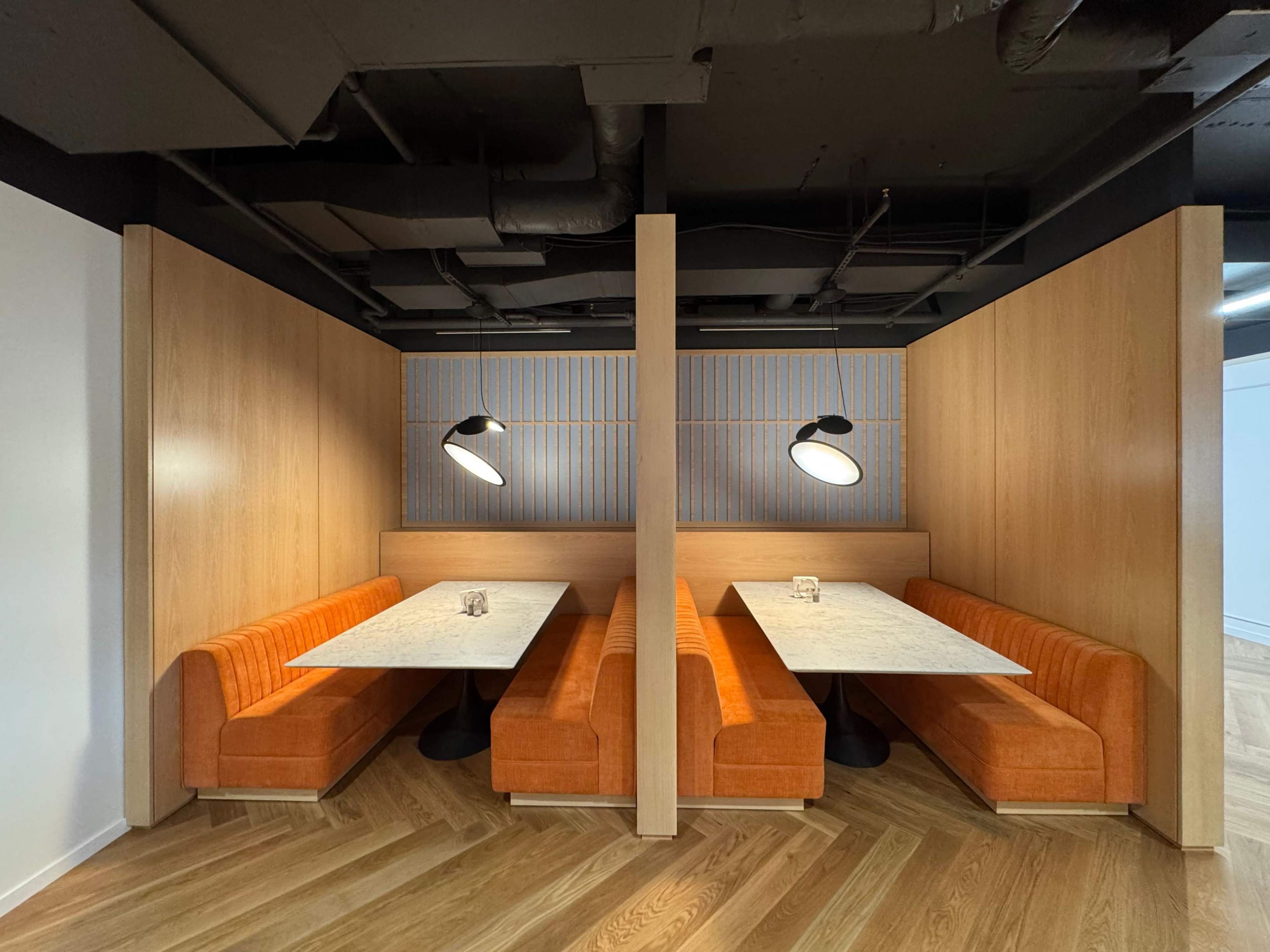 The image shows two adjacent booths with orange seating and marble tables in a modern interior design, accented by overhead lighting.