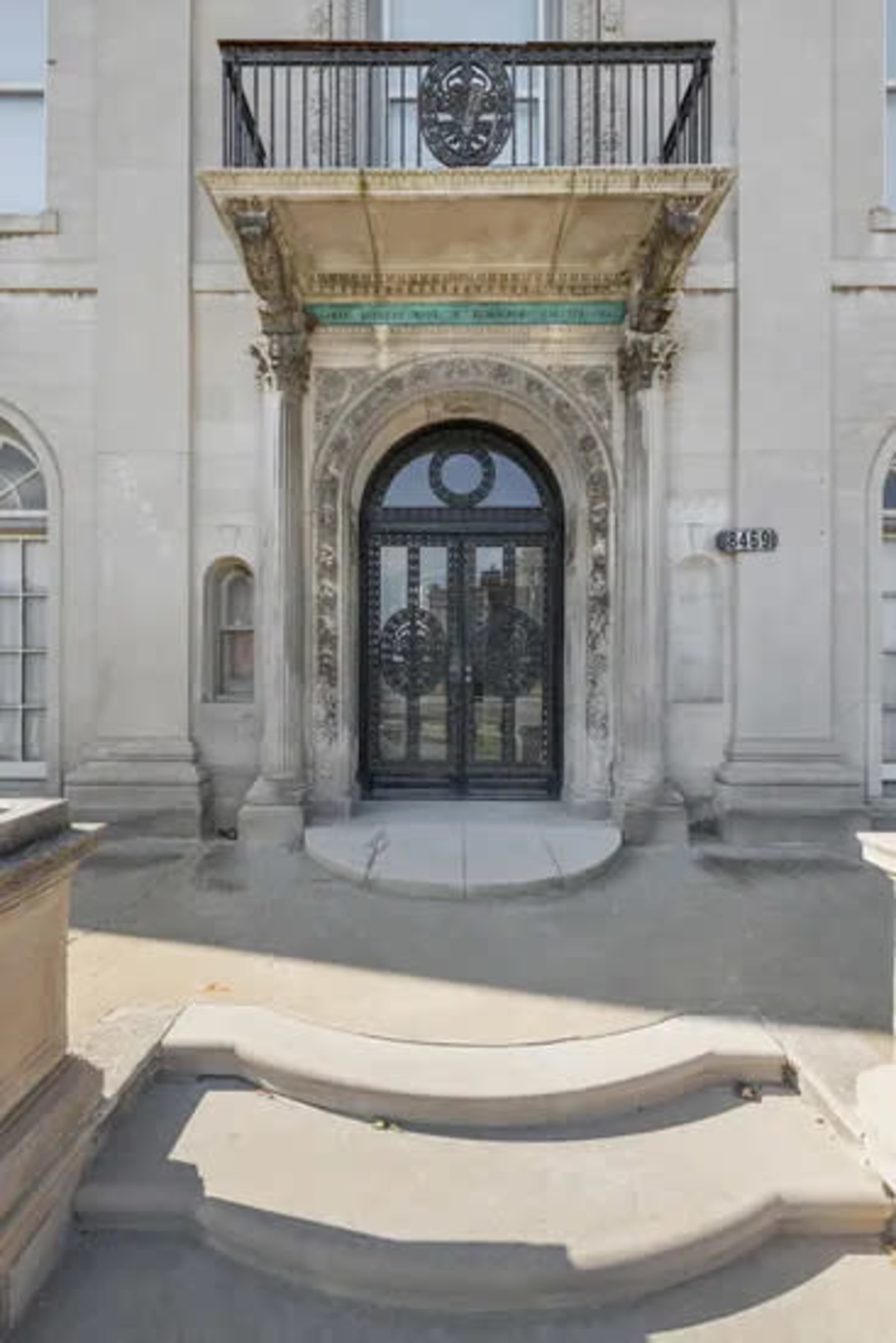 The image shows an ornate entrance with a black wrought iron door and decorative architectural features, flanked by tall windows.