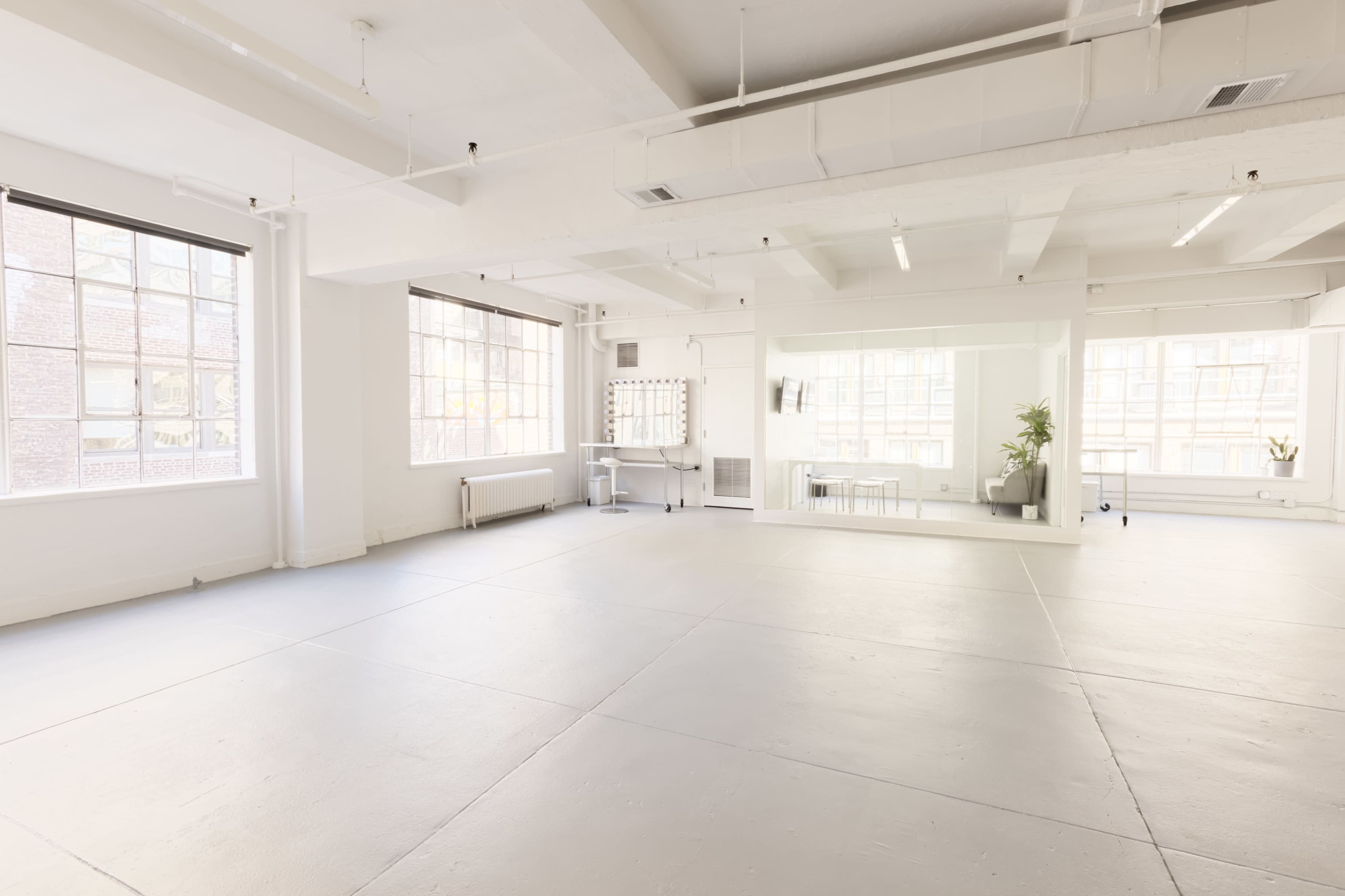 A spacious, brightly lit interior room with large windows, grey flooring, and minimalist decor.