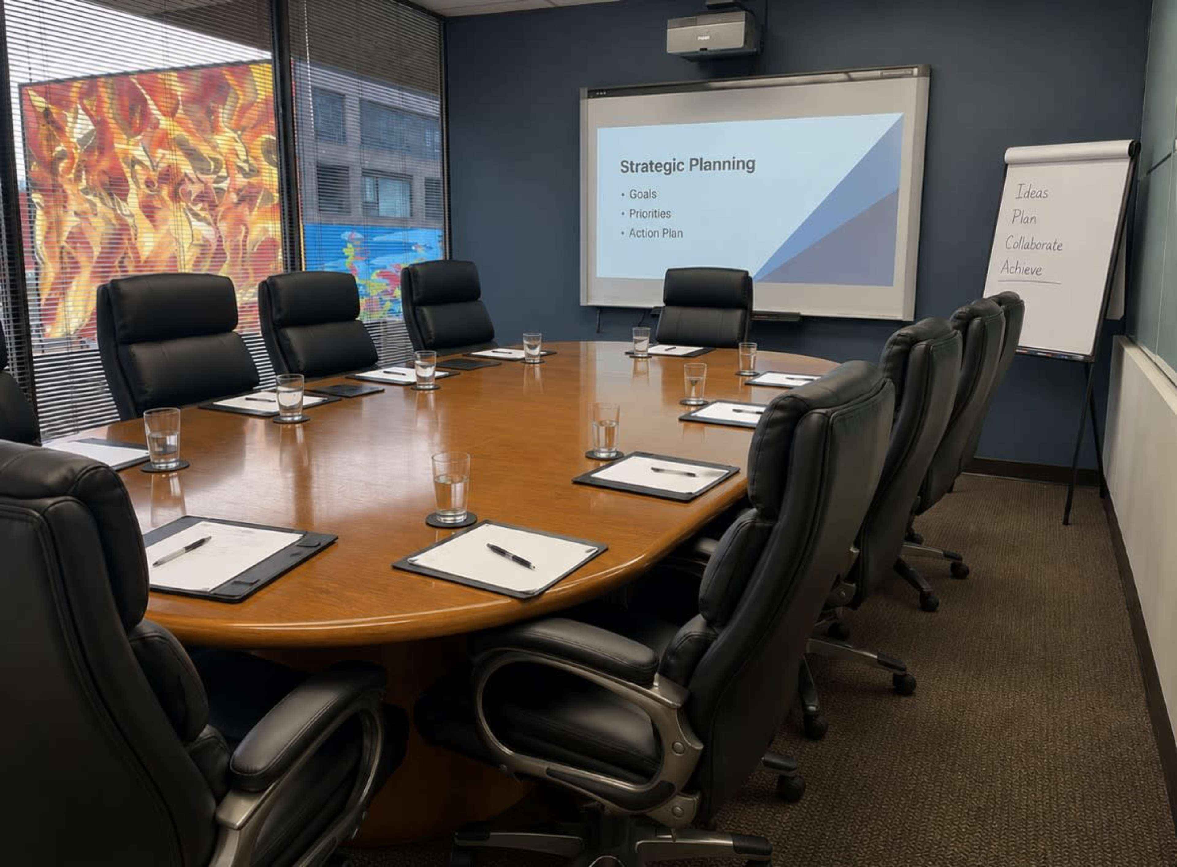 A conference room is set up with a large round table, ergonomic chairs, presentation screen, and flip chart, ready for a strategic planning meeting.