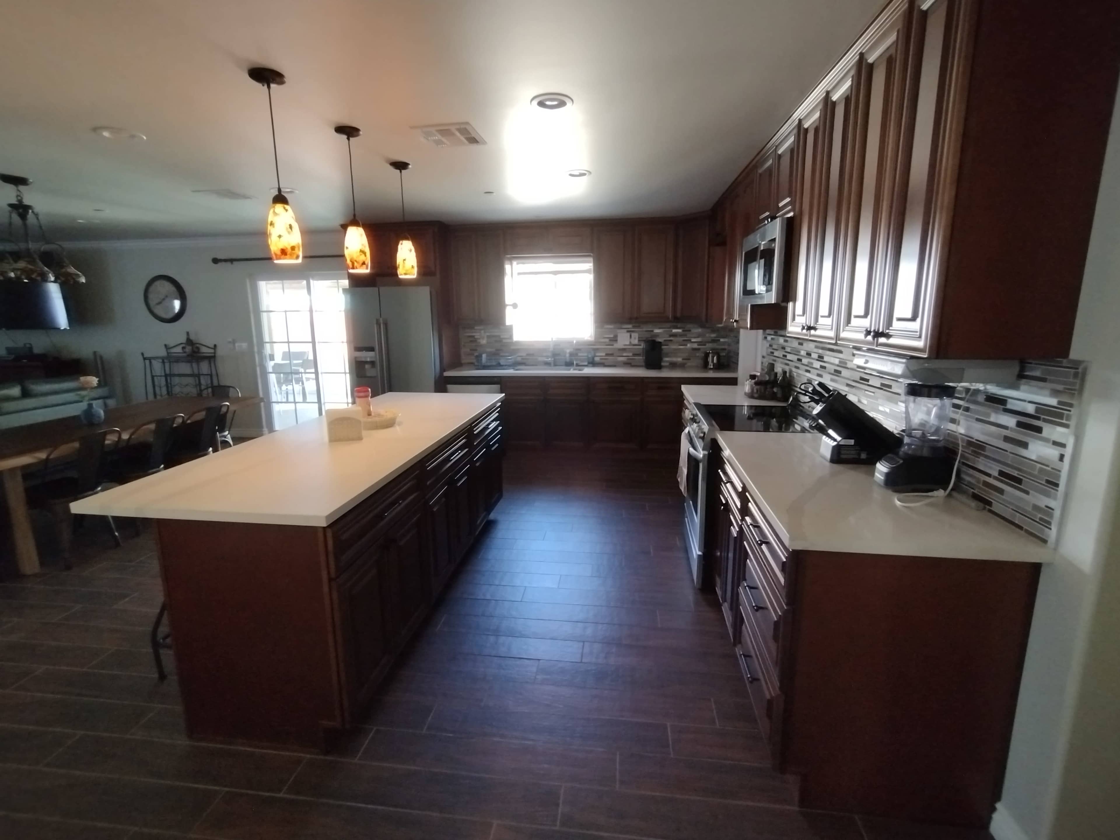 A modern kitchen with dark wood cabinetry, a central island, and a light-colored countertop, along with stainless steel appliances and tile flooring.