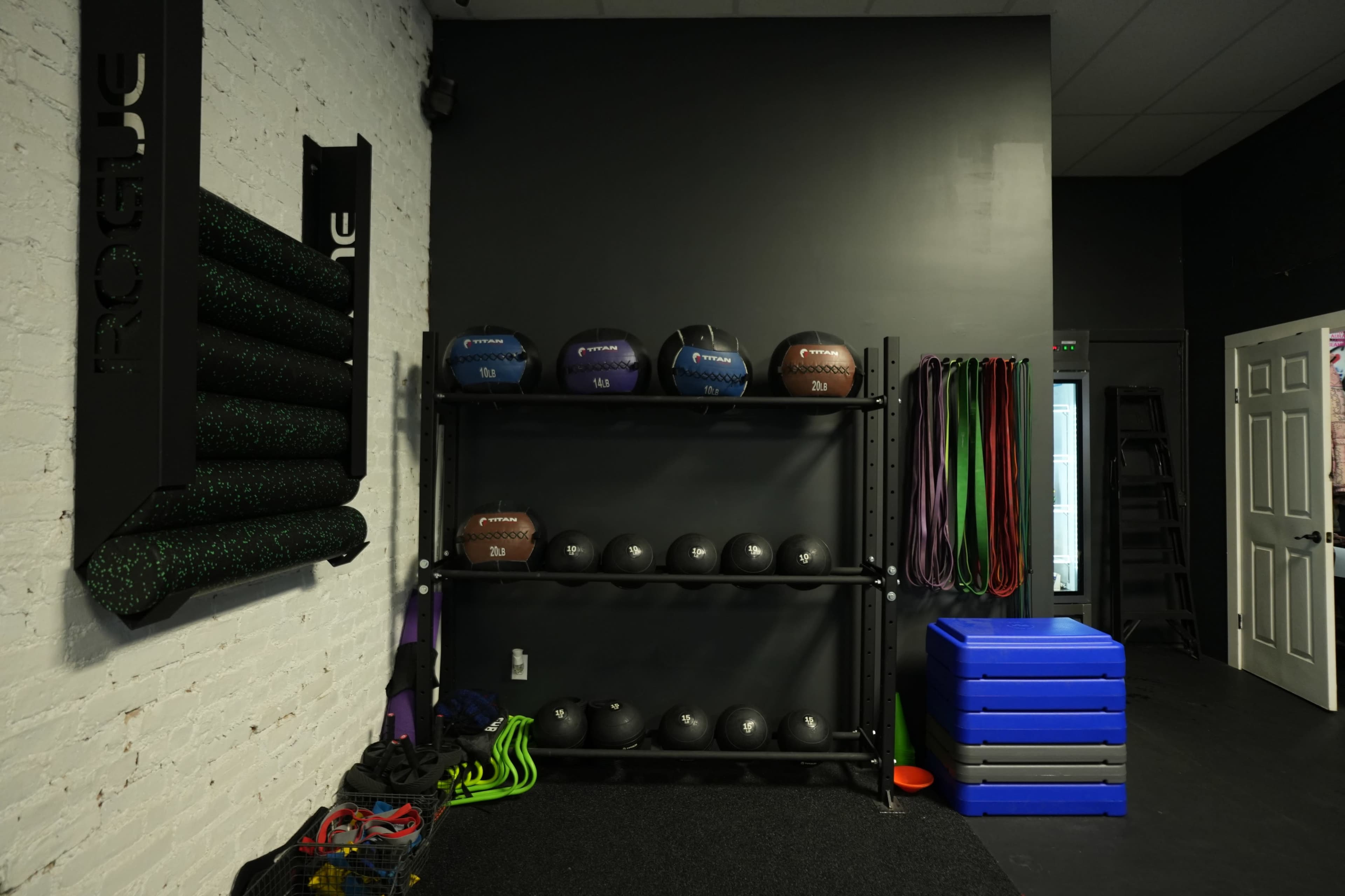 A gym corner featuring a rack of medicine balls, storage for exercise mats, and a variety of resistance bands.